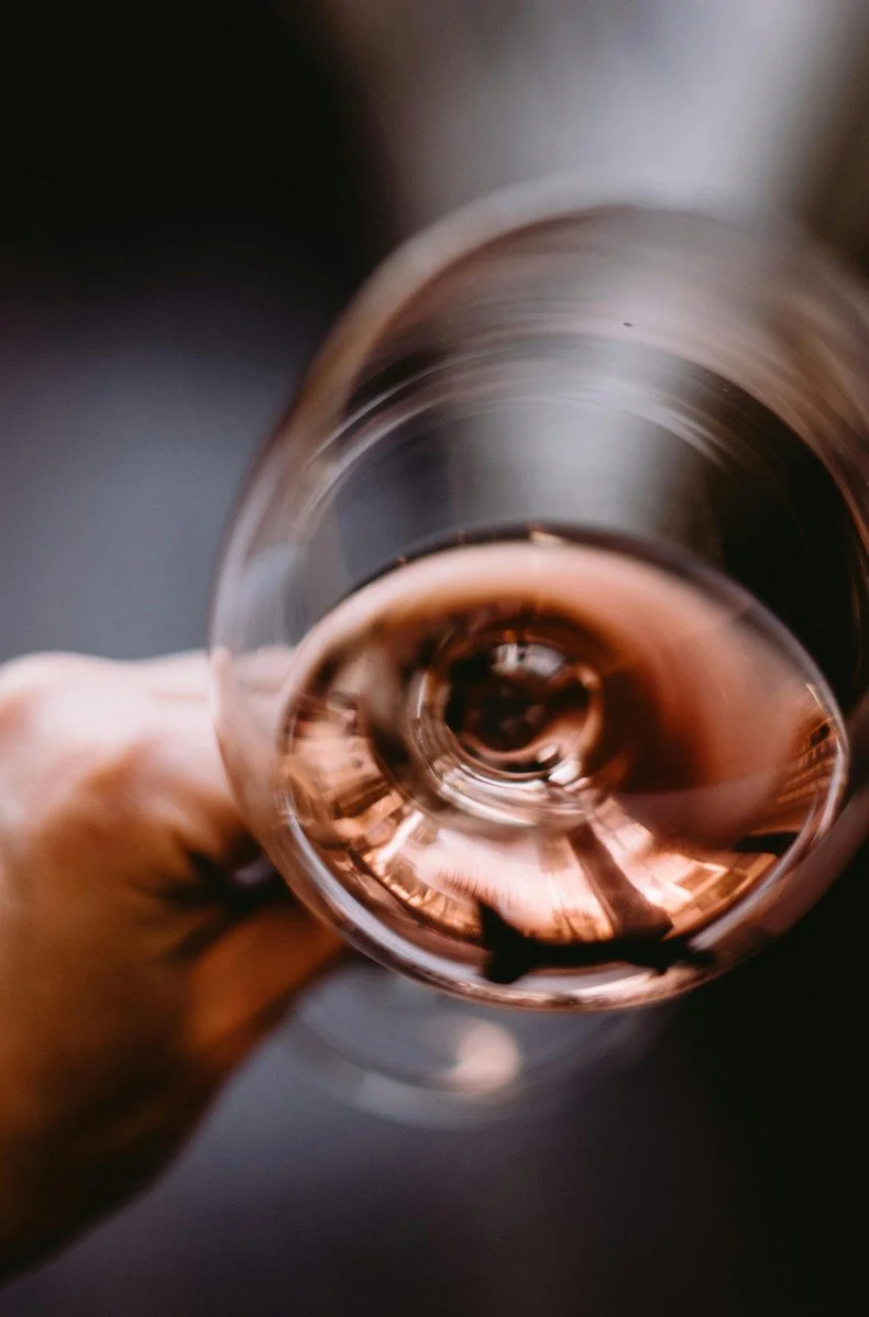 A hand holding a glass of rosé wine, viewed from above.