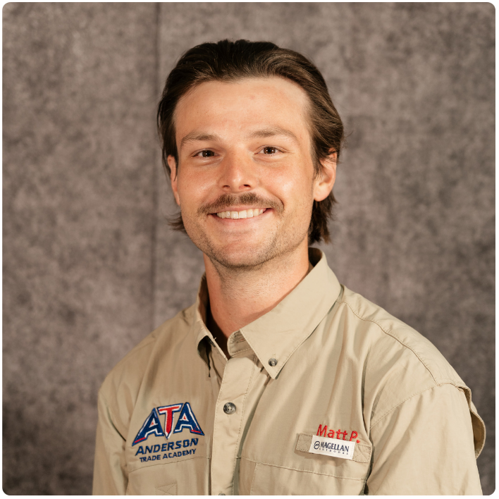 A man with brown hair and a mustache smiling, wearing a beige button-up shirt with patches that read "ATA Anderson Trade Academy" and "Matt P" against a gray background.