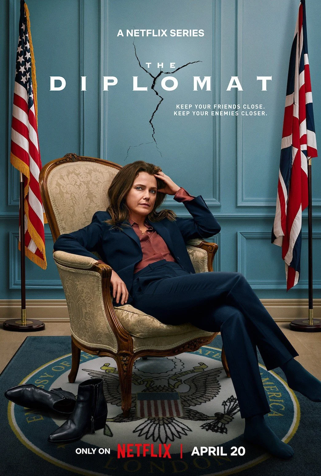 Poster for the Netflix series 'The Diplomat' featuring a woman sitting confidently in a government office with American flags on either side, a cracked wall behind her, and a presidential seal on the floor, with the series release date April 20.