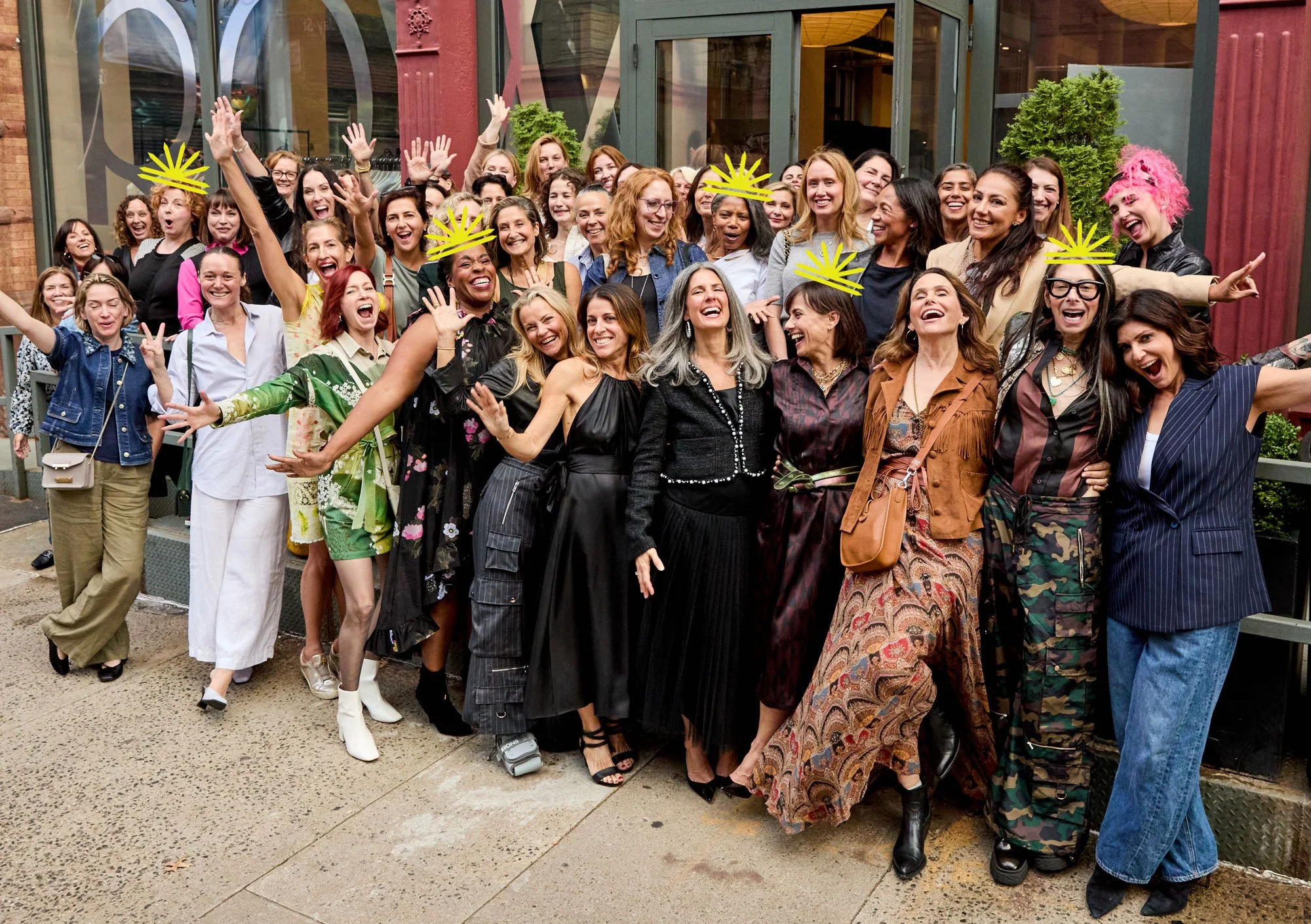 Group of women, including Tamsen Fadal, Heidi Clements, Stacy London, Constance Zimmer, Julie Flakstad, and Abby Epstein, gathered outside a building, smiling and celebrating, with some wearing yellow crowns.
