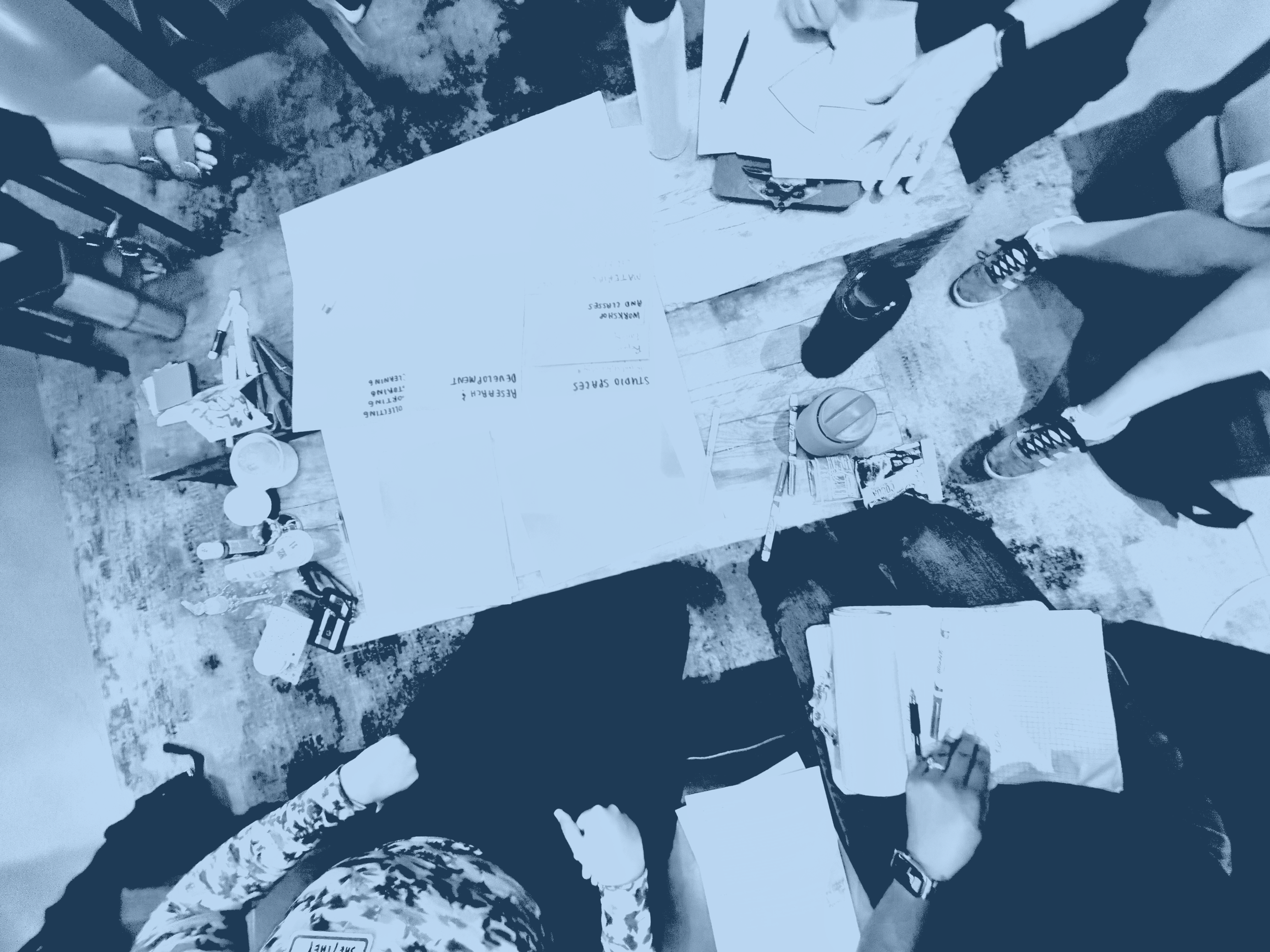 Overhead view of people gathered around a table with papers, notebooks, and art materials.