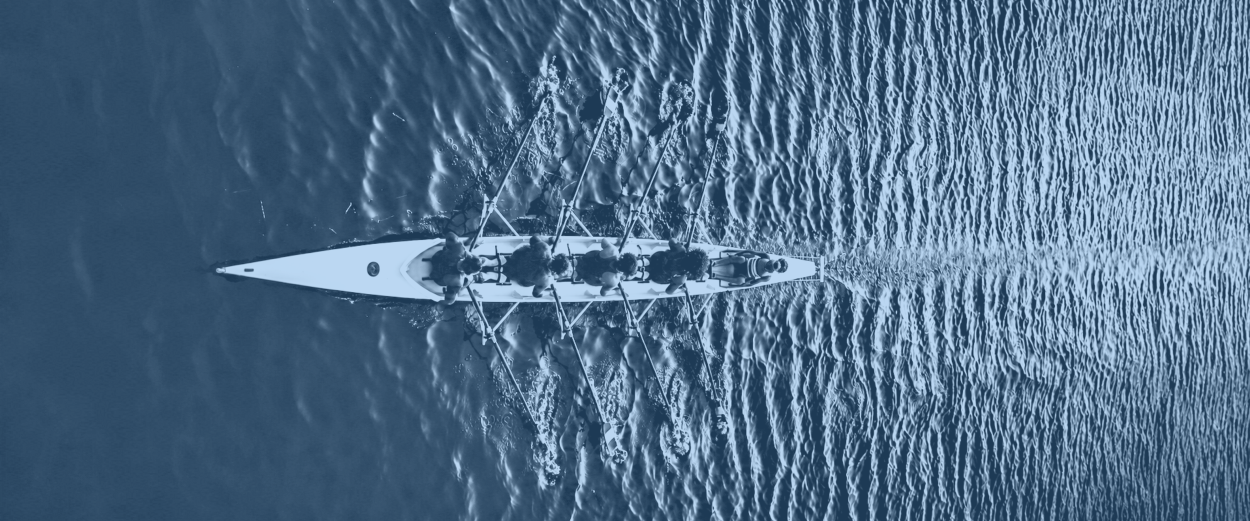 An aerial view of a rowing team in a white boat on the water, with seven rowers and a coxswain.