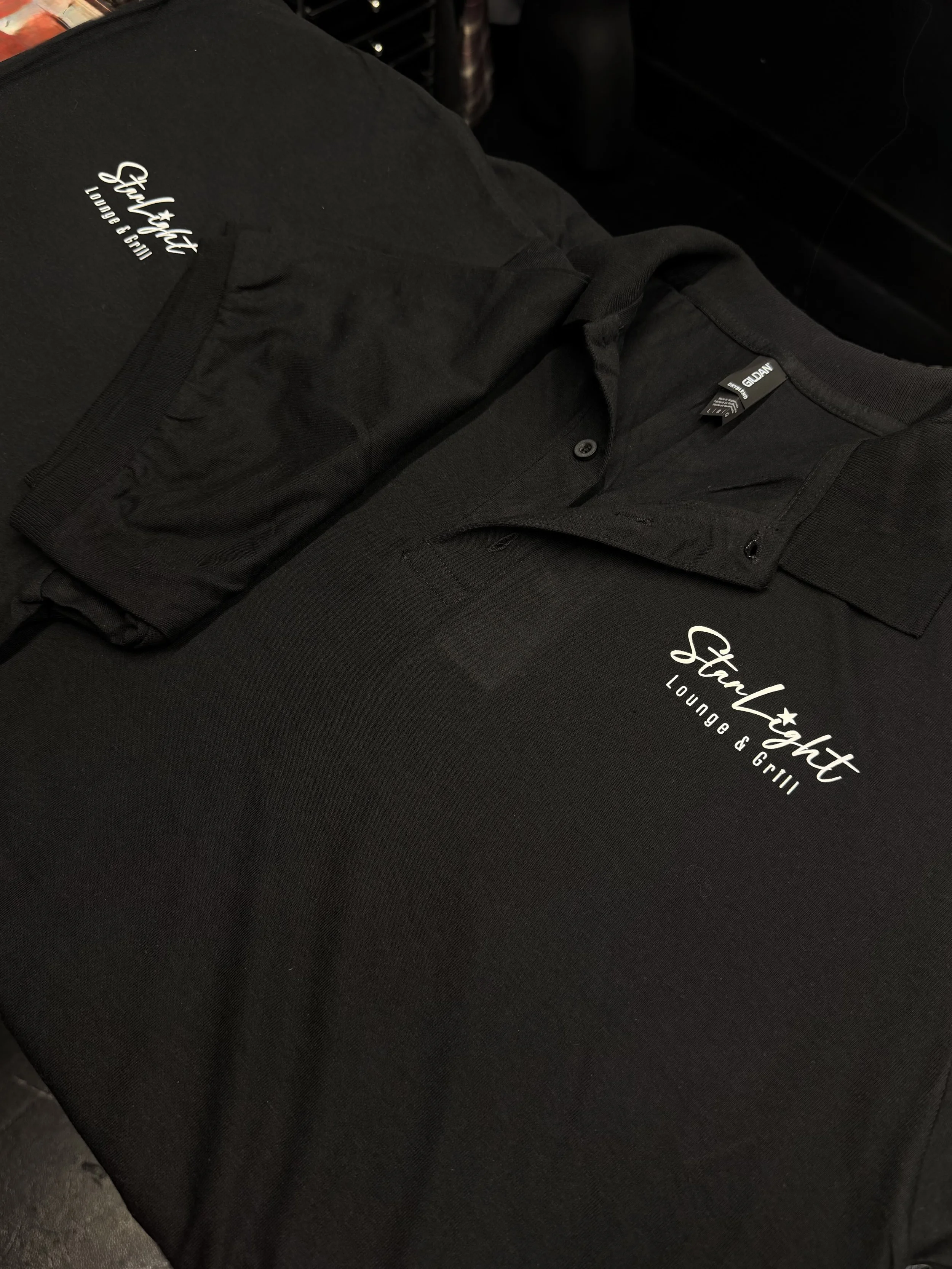 Black tablecloth with the words "Stylight Lounge & Grill" printed in white, covering a table with black clothing items placed on top.