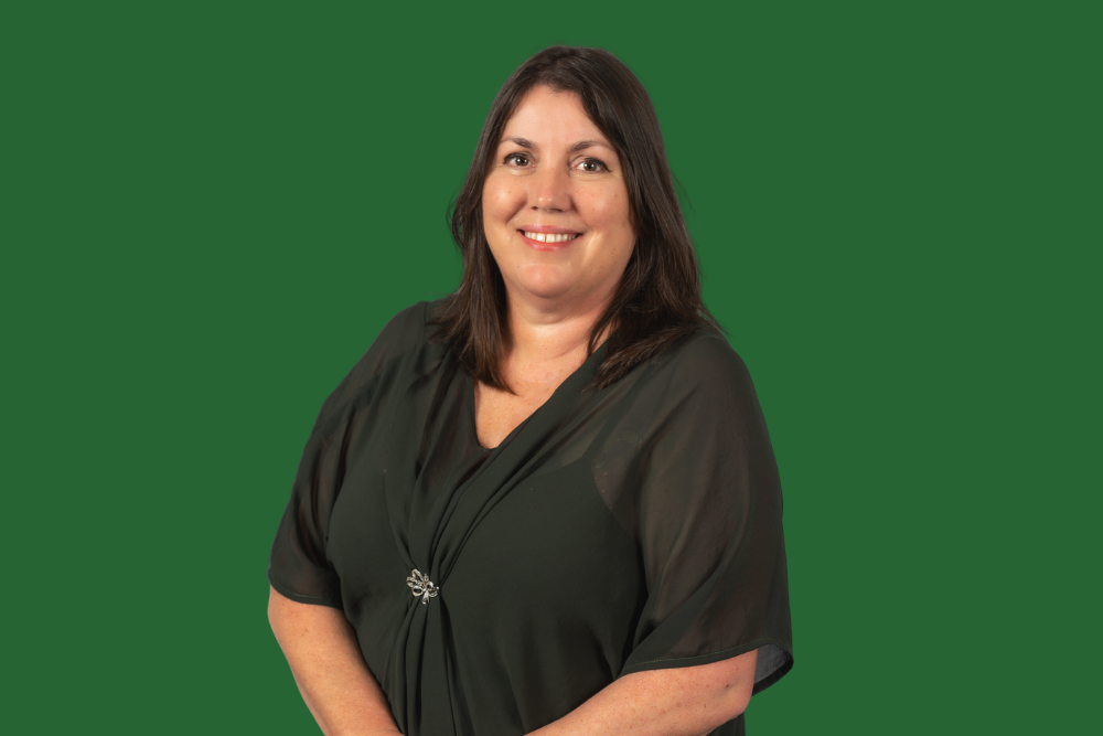 A woman with shoulder-length dark hair smiling, wearing a black blouse with a decorative brooch, against a green background.