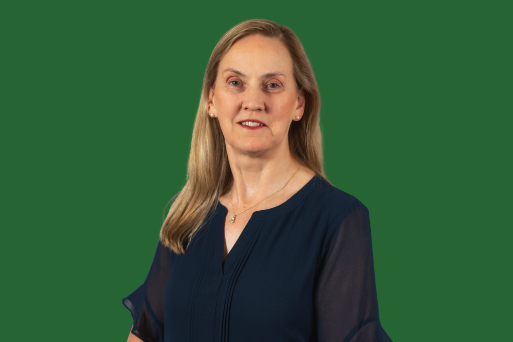 A woman with blonde hair wearing a navy blouse standing against a green background.