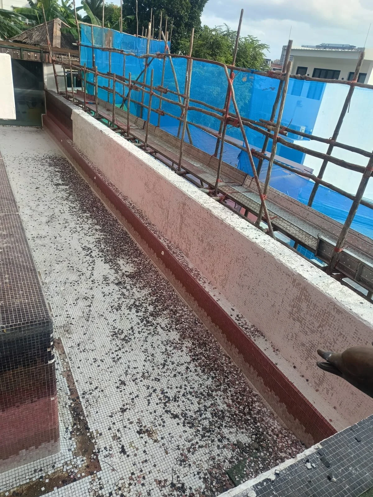 Balcony with black scattered debris on mosaic tile floor, pink painted concrete wall, and scaffolding covered with blue tarp outside.