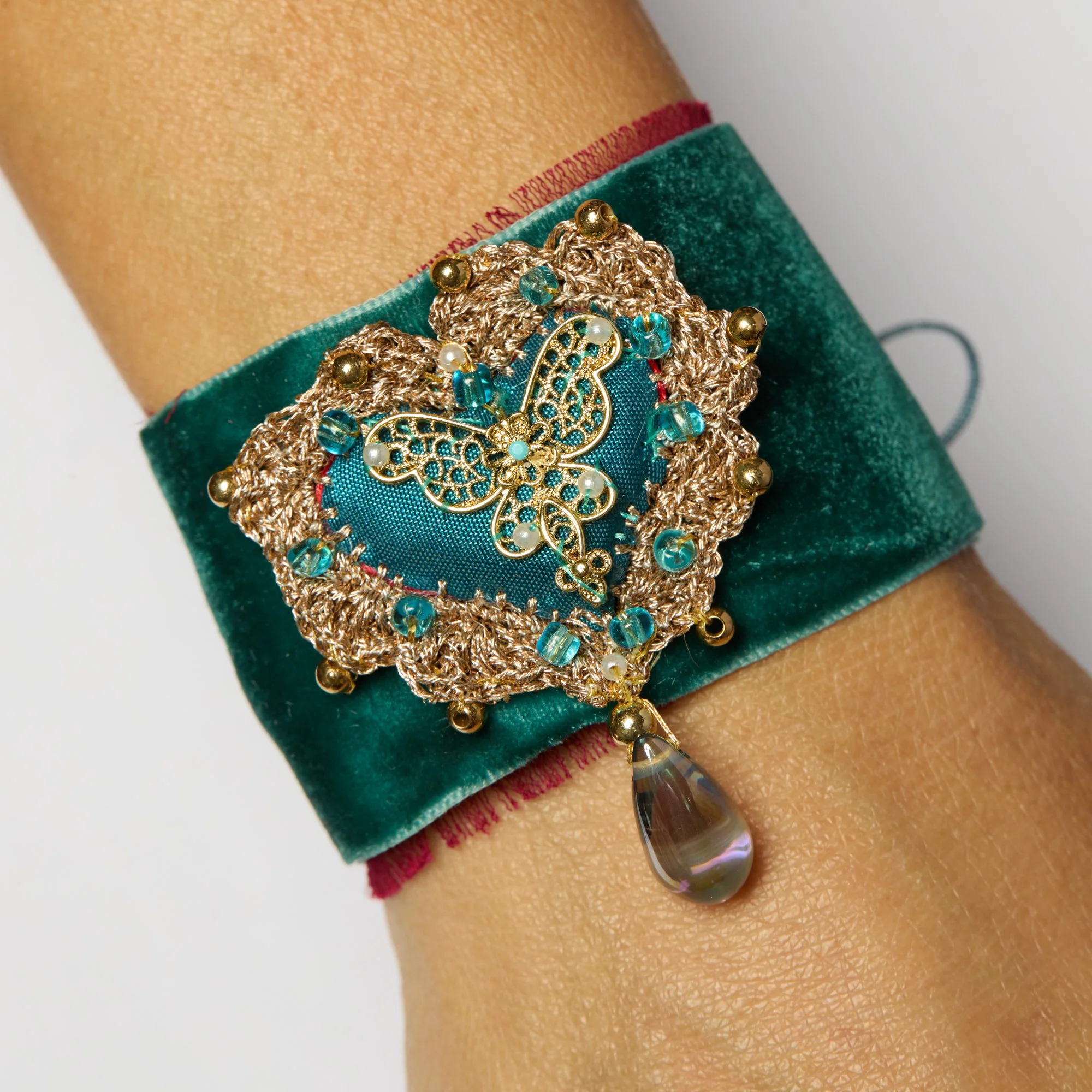 Close-up of a skin bracelet with intricate gold and turquoise butterfly design, turquoise fabric, and dangling beads.