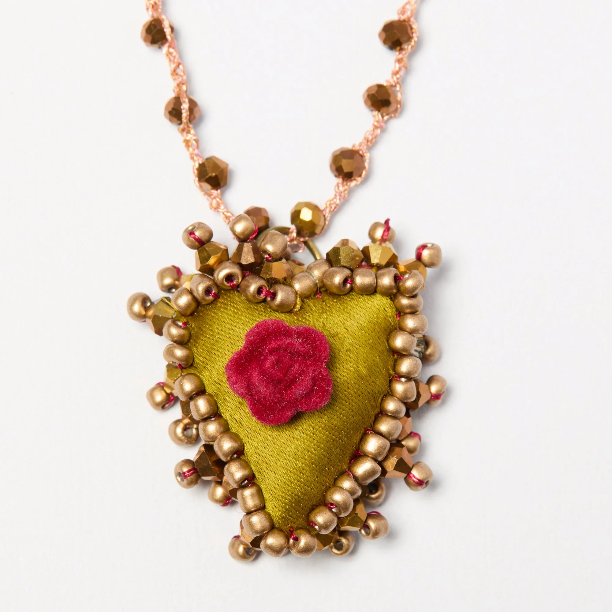 Close-up of a decorative necklace with golden beads, pink threads, and fabric with a red heart pattern.