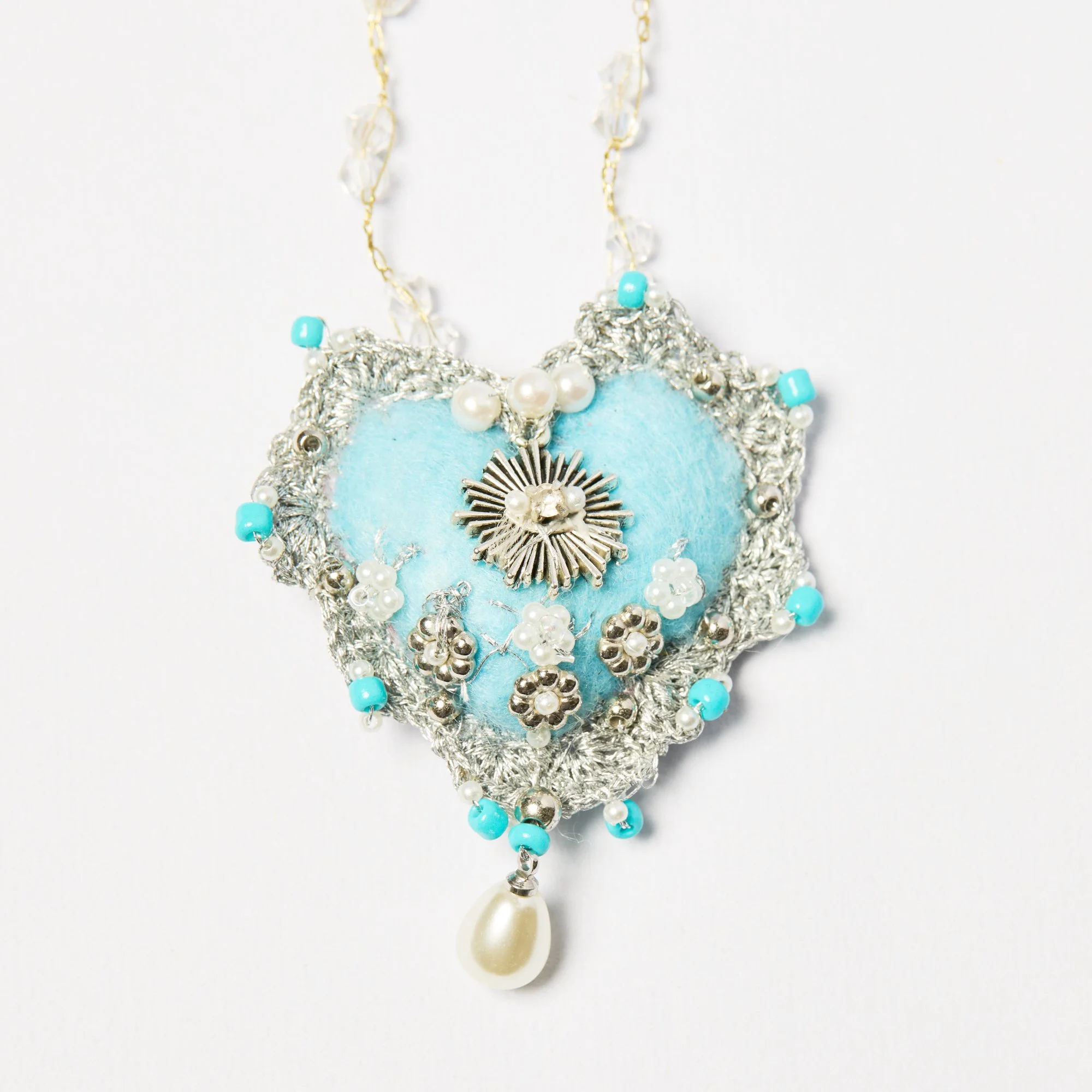 A close-up of a decorative necklace with silver, turquoise, and pearl beads, featuring a silver star charm, set against a white background.