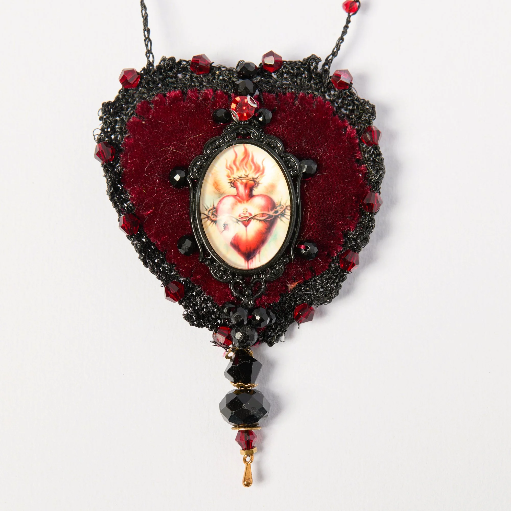 Ornate necklace featuring a pendant with a detailed illustration of a human heart, adorned with red and black beads, velvet accents, and intricate black and gold metalwork.