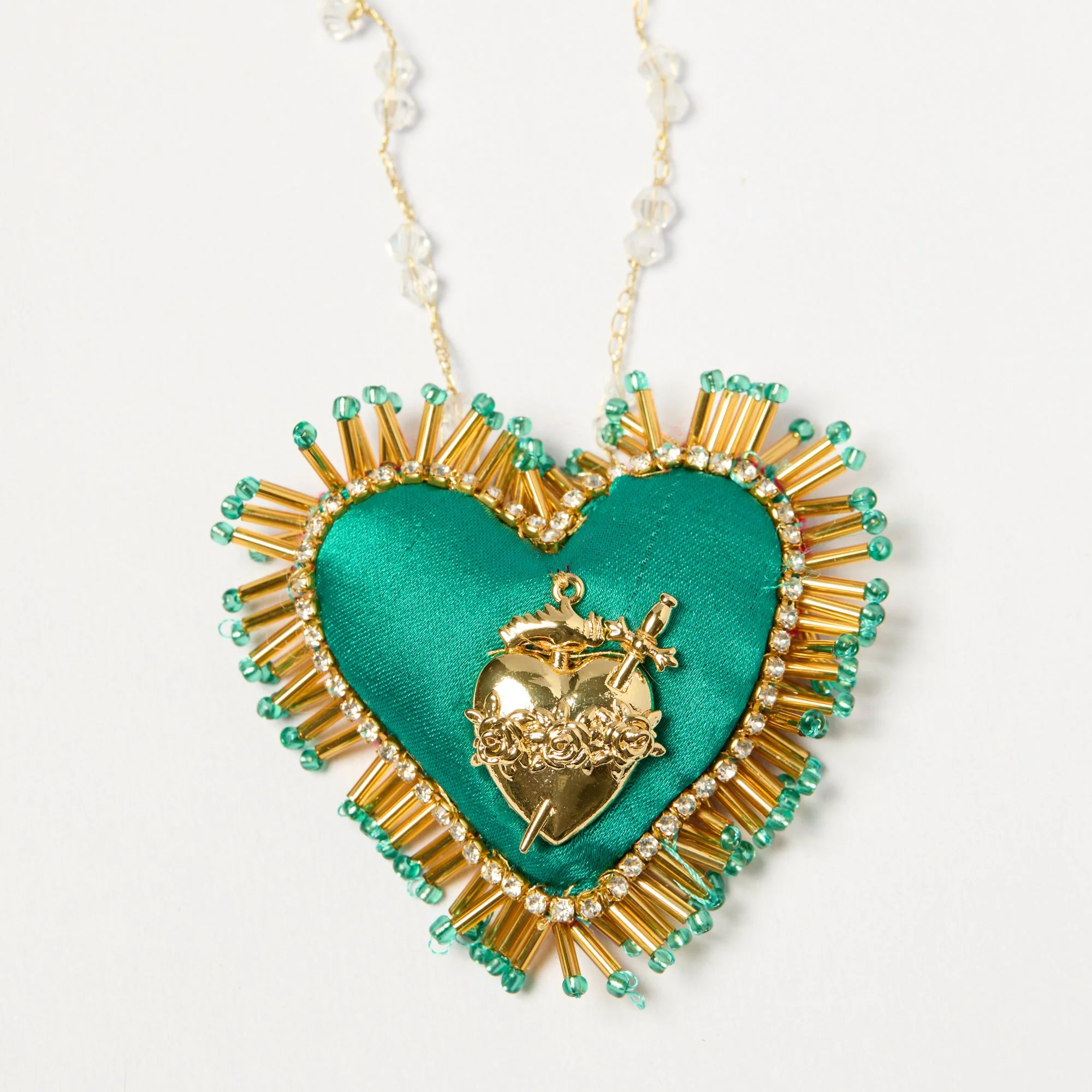 Close-up of decorative handmade jewelry featuring green fabric hearts outlined with gold beads, quartz beads, and gold charms, hanging on a white background.