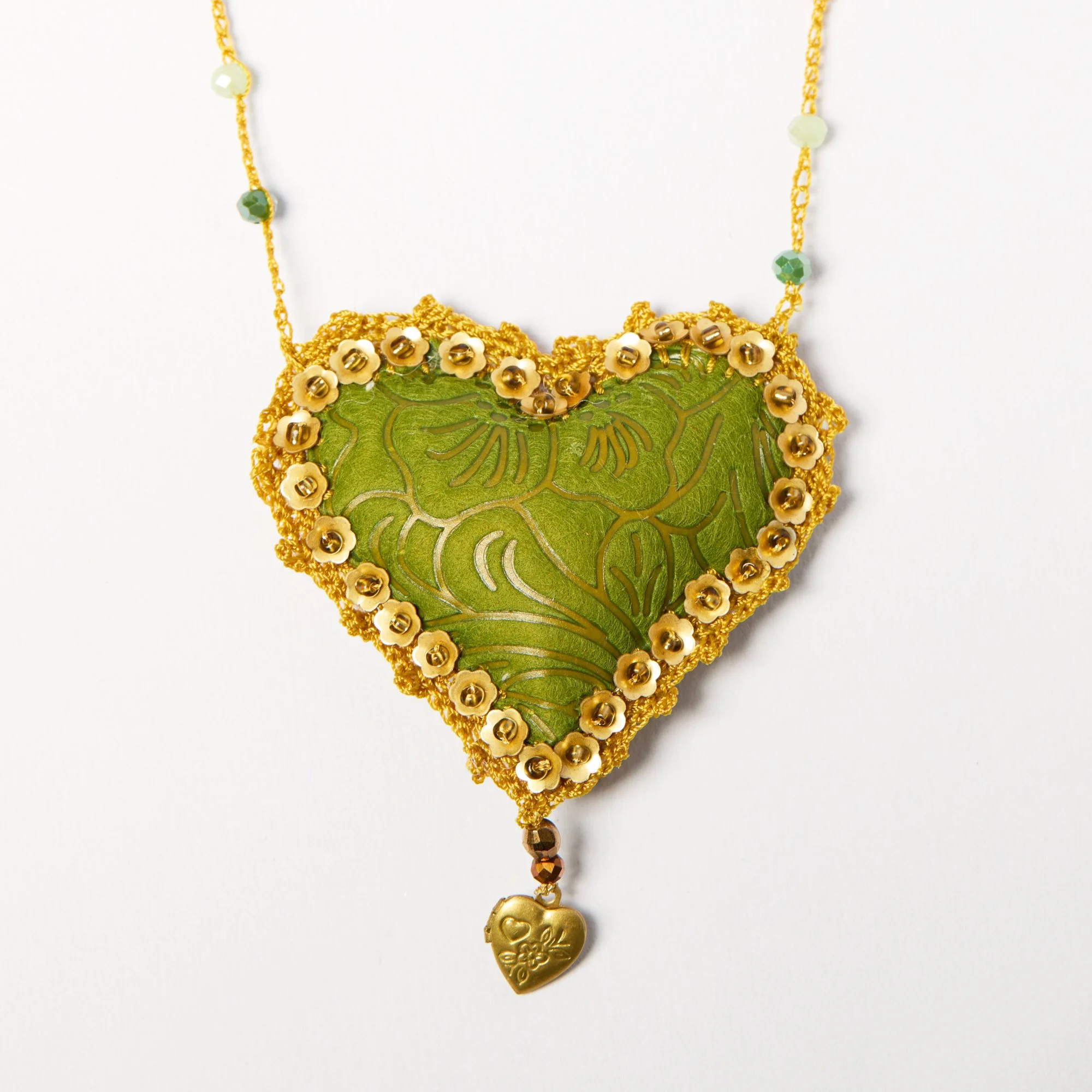 Close-up of a handmade gold and green necklace with small flowers, green and gold beads, and a heart-shaped pendant.