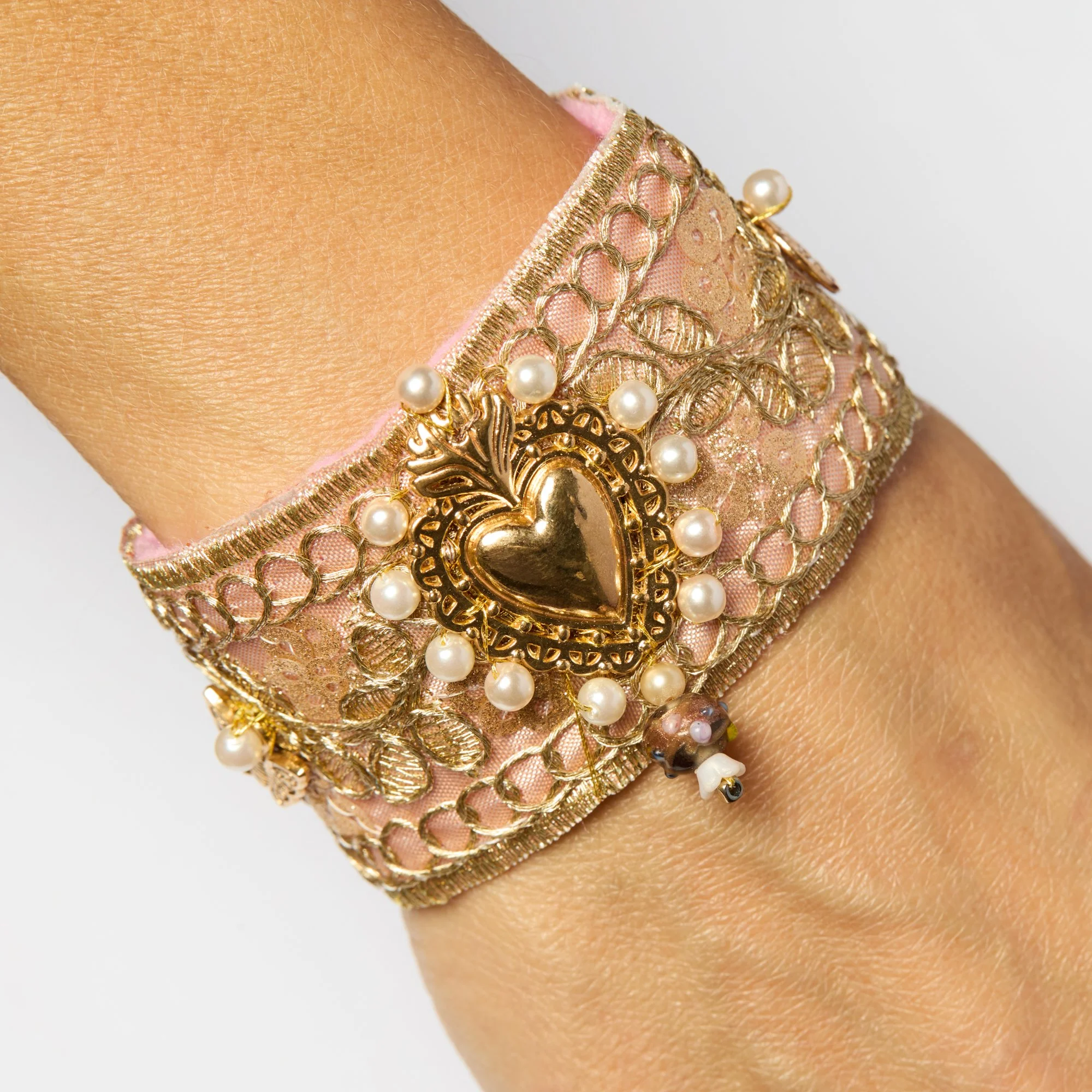 Close-up of a person's wrist adorned with a ornate gold and pink bracelet decorated with pearls and gold filigree details.
