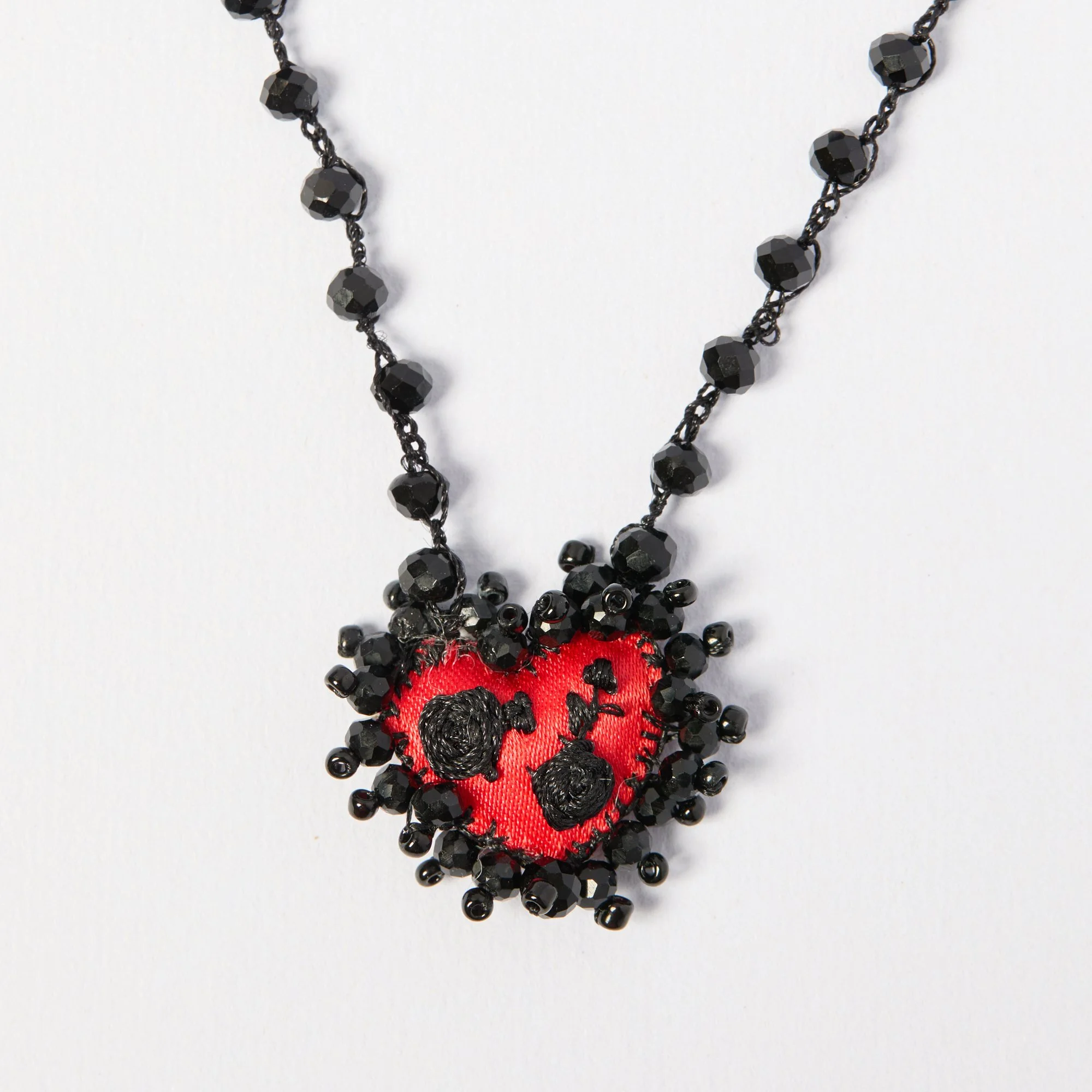 Black beaded necklace with a red fabric pendant featuring black embroidered designs.
