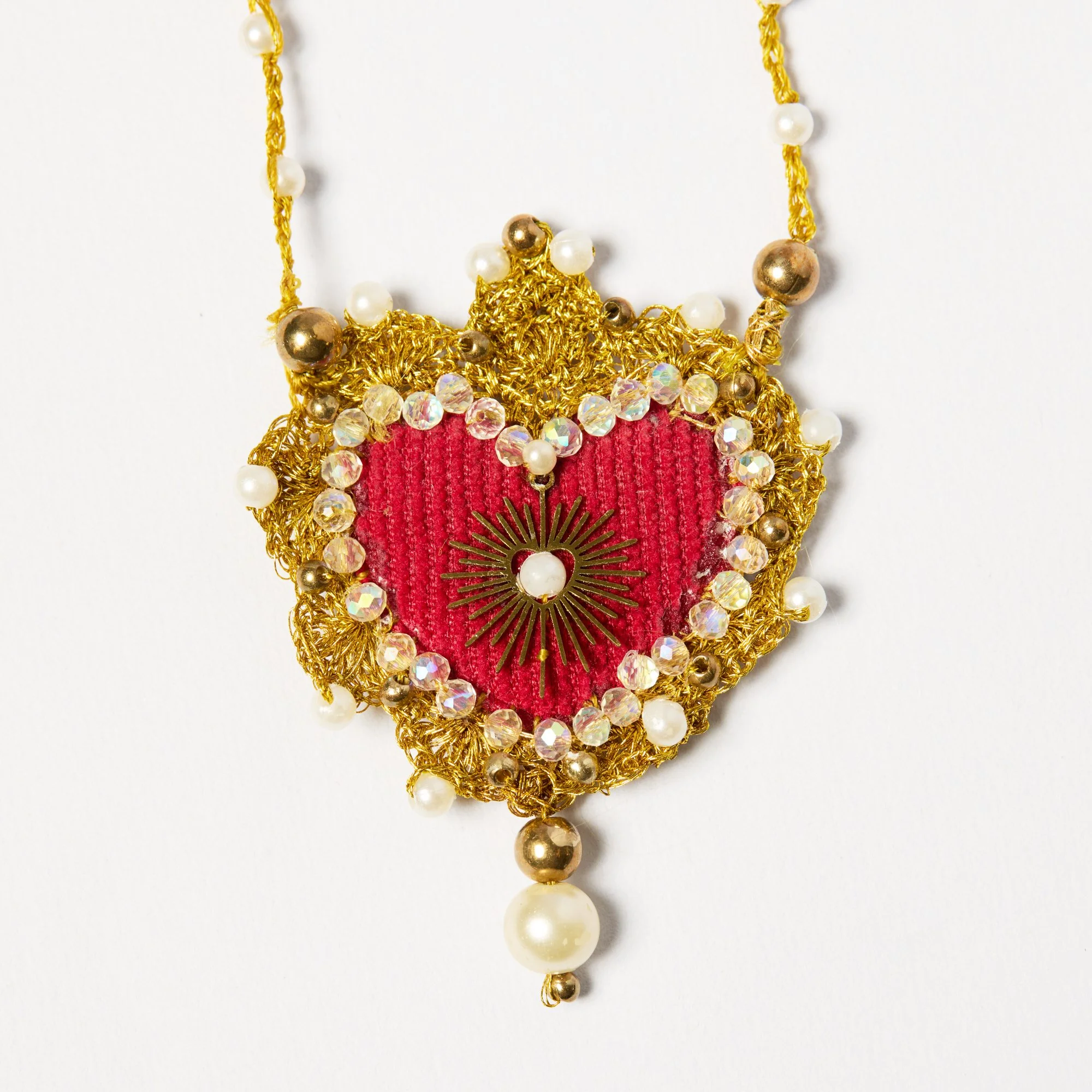 Close-up of a decorative necklace with gold, pearl, and rhinestone accents hanging against a white background.