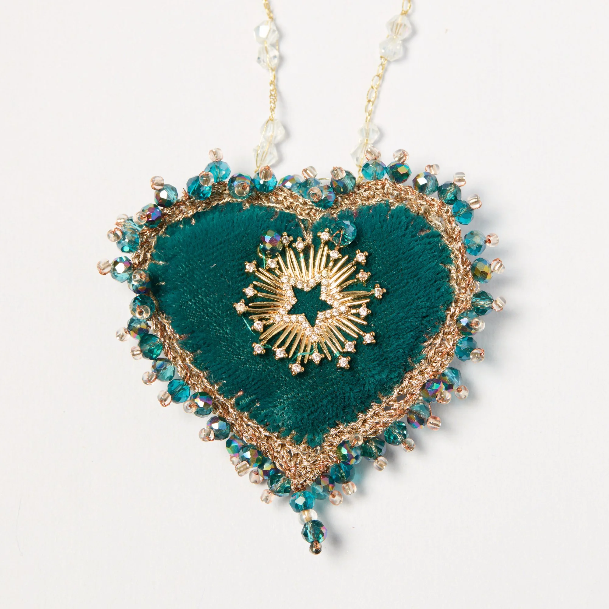 Close-up of a handmade decorative pendant with teal fabric, gold accents, and clear beads arranged in an intricate pattern.