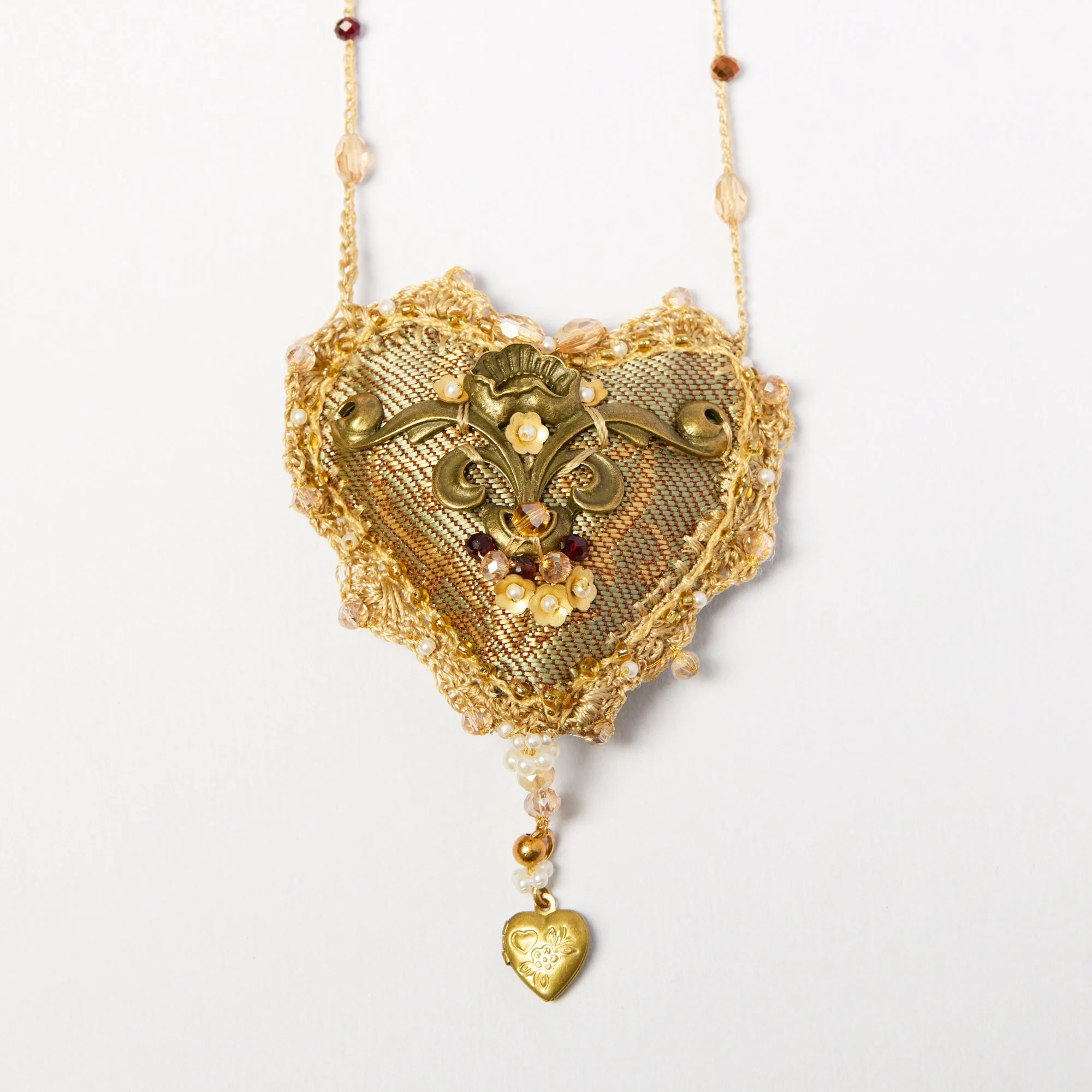 Close-up of a gold necklace with intricate designs, pearls, and heart-shaped pendants, hanging against a white background.