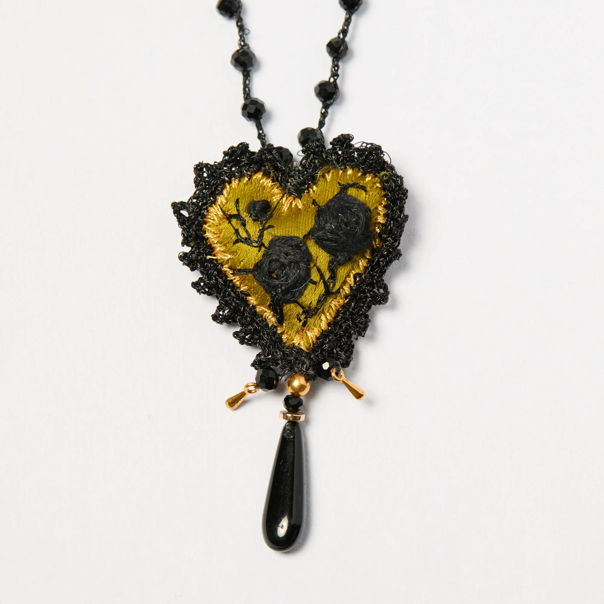 A black and gold handmde embroidered necklace with a black pendant hanging from a beaded chain.