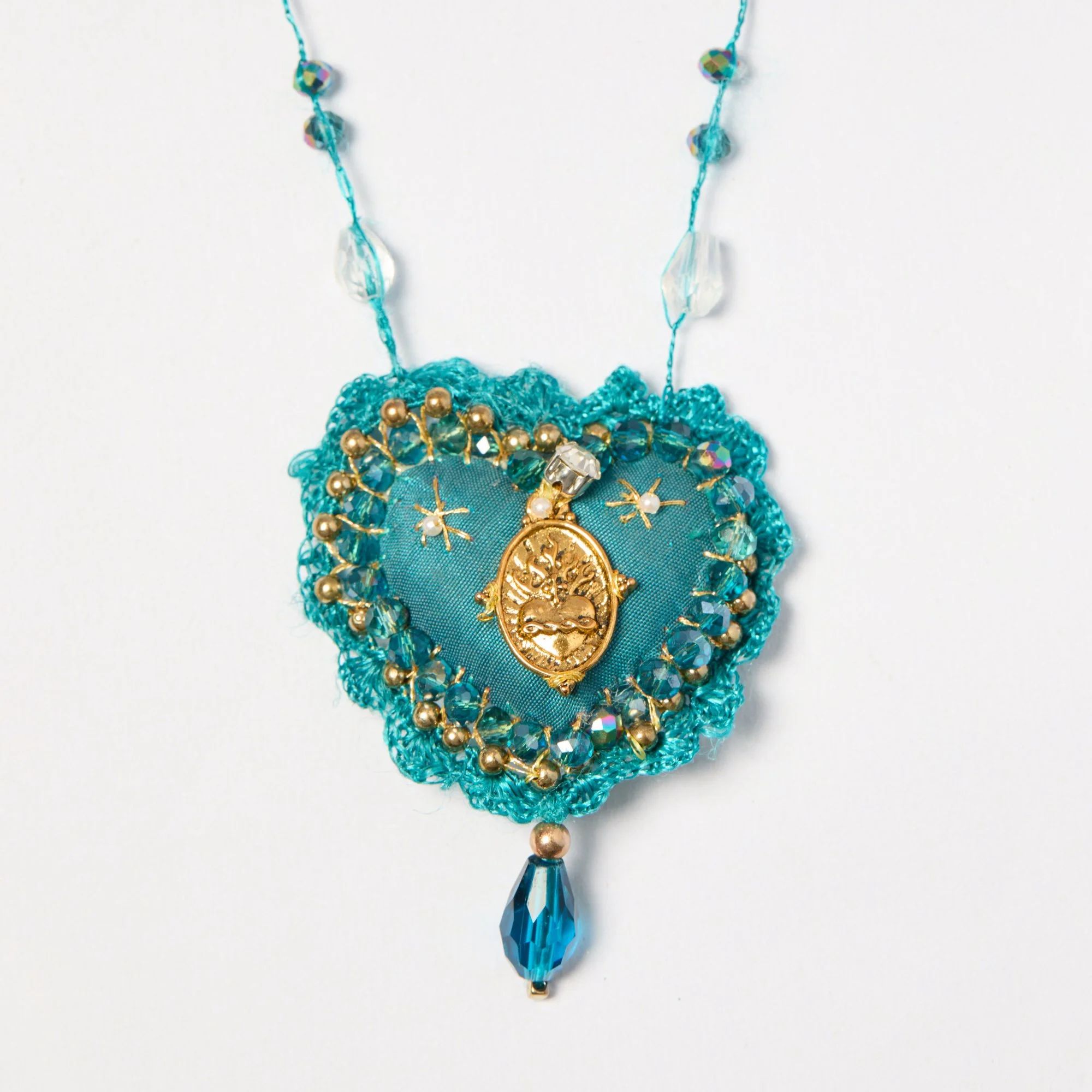 Close-up of a jewelry necklace featuring blue and gold beads, a blue fabric base, and a large blue teardrop-shaped pendant.