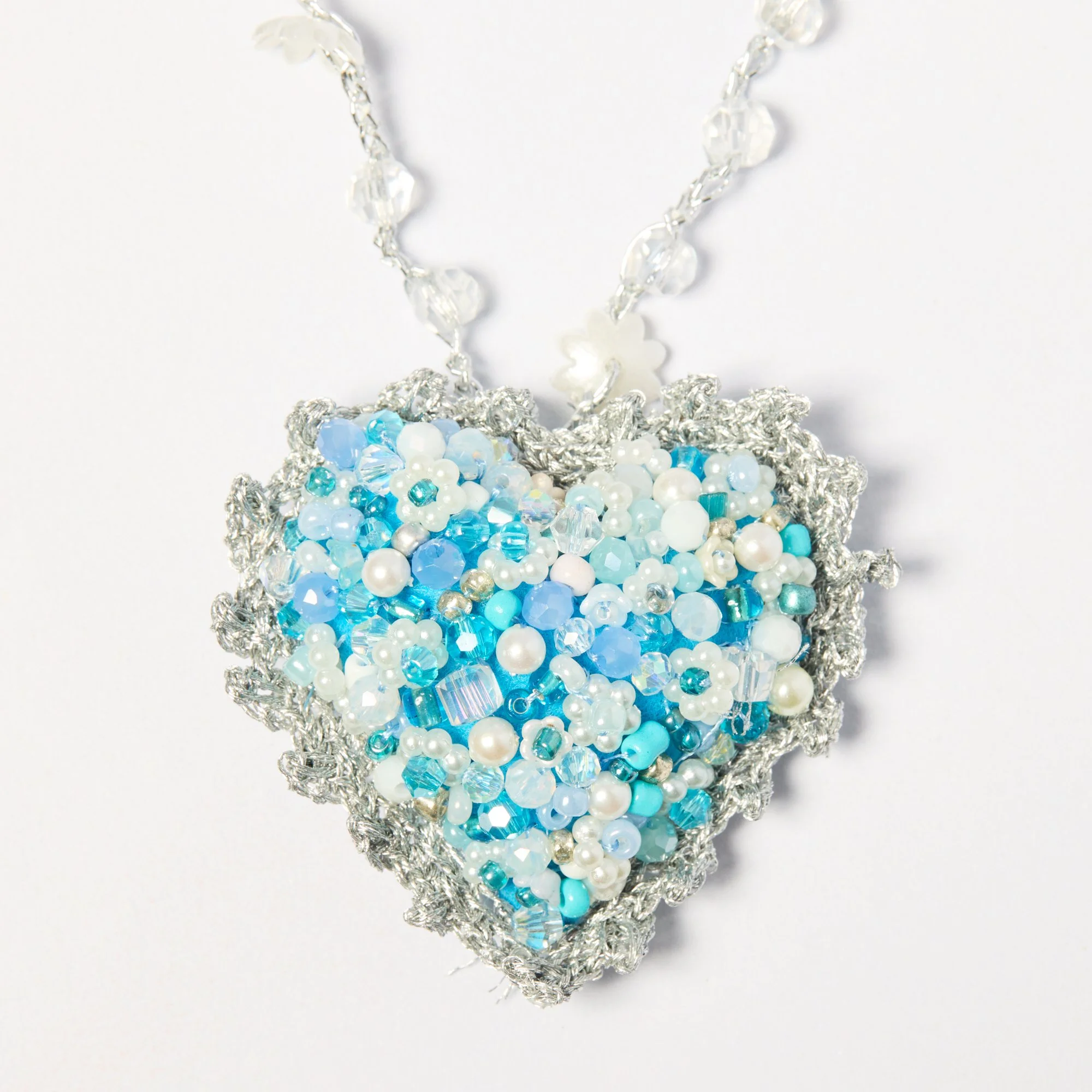 Close-up of a beaded jewelry piece with blue, white, and clear beads, and a silver chain, placed on a white background.