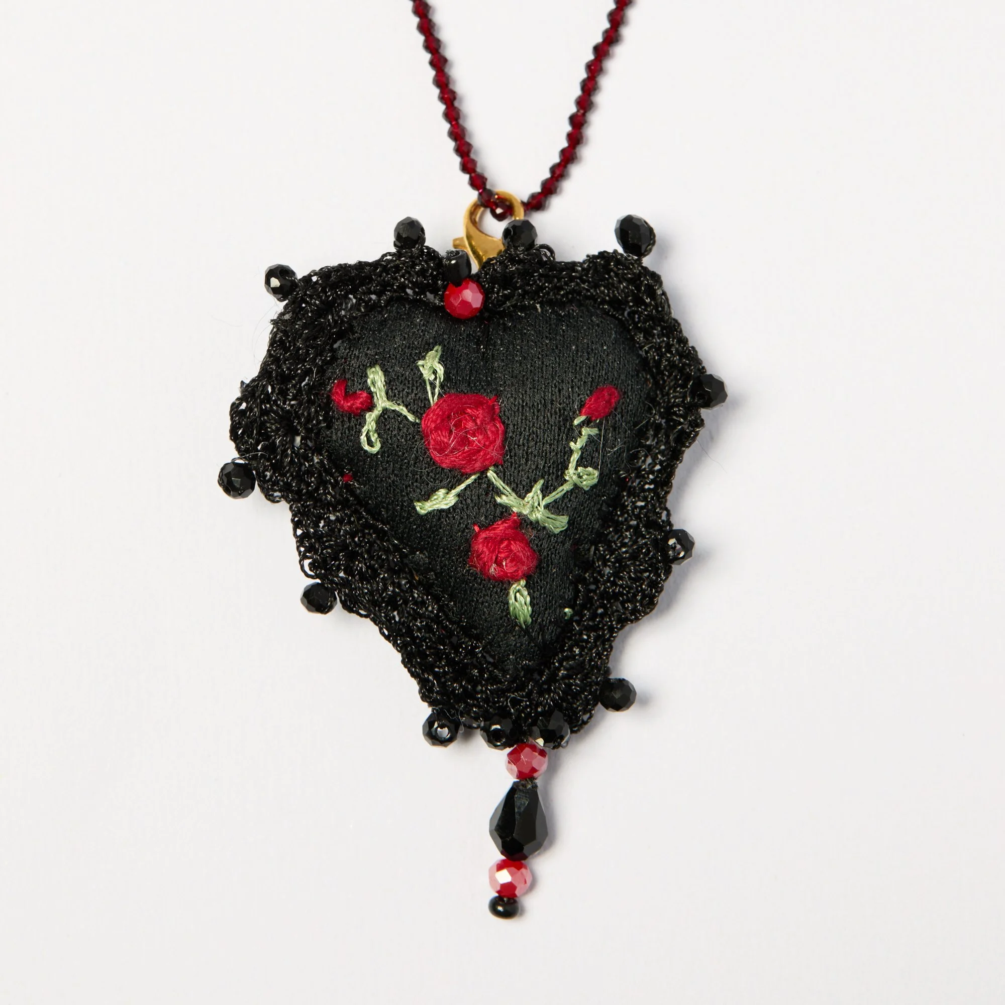 A black beaded pendant necklace with red and black beads, featuring embroidered red roses and green leaves on a black fabric background.
