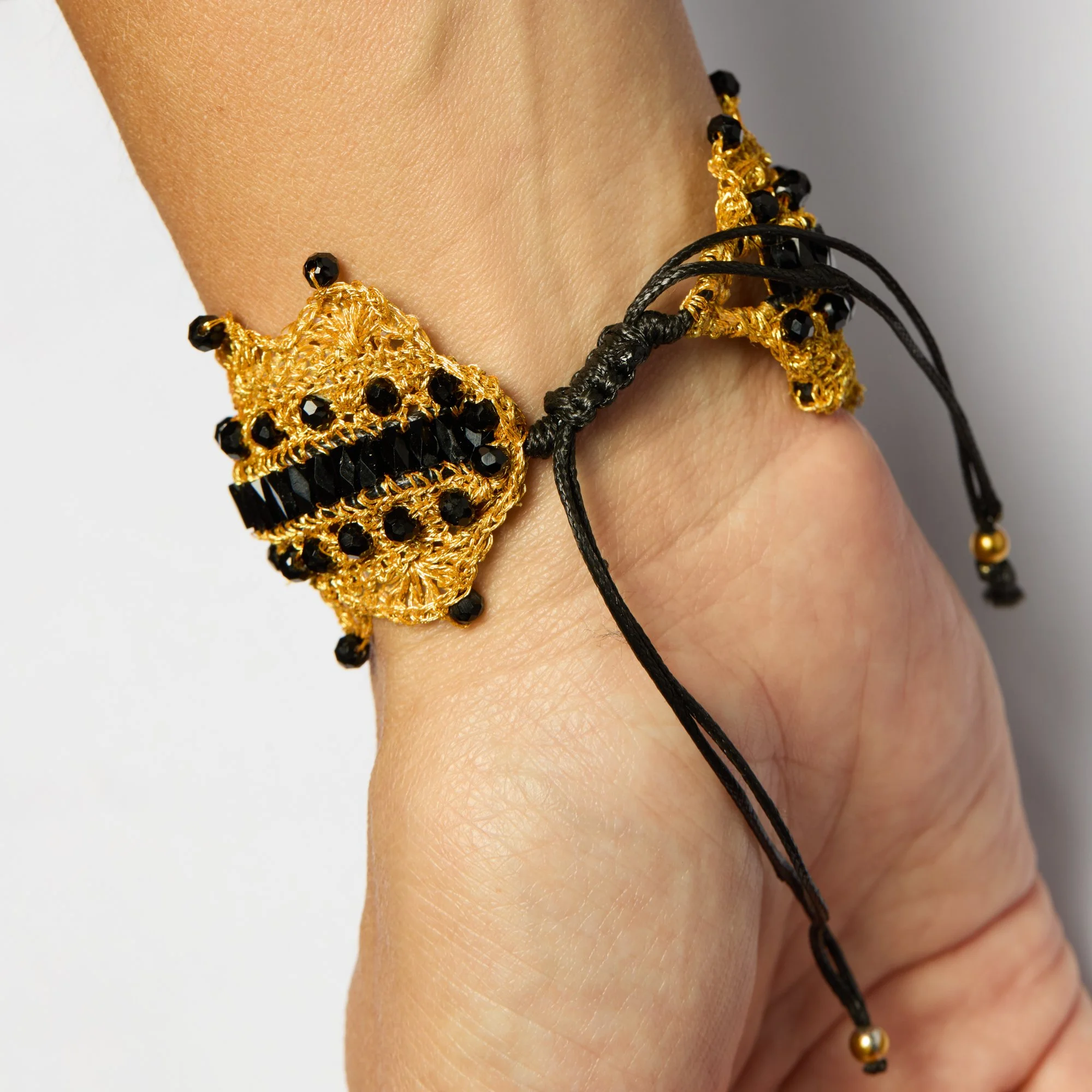 Close-up of a person's wrist wearing a gold and black beaded bracelet and a black braided cord bracelet.