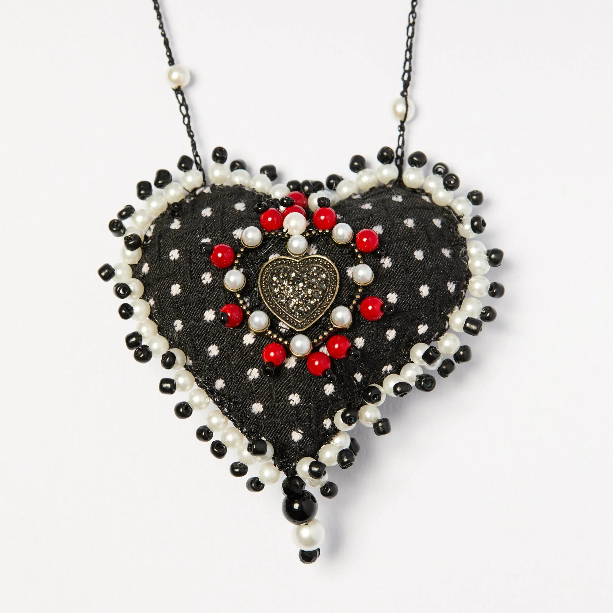 Close-up of a decorative necklace with black, white, and red beads, featuring a heart-shaped pendant in the center.