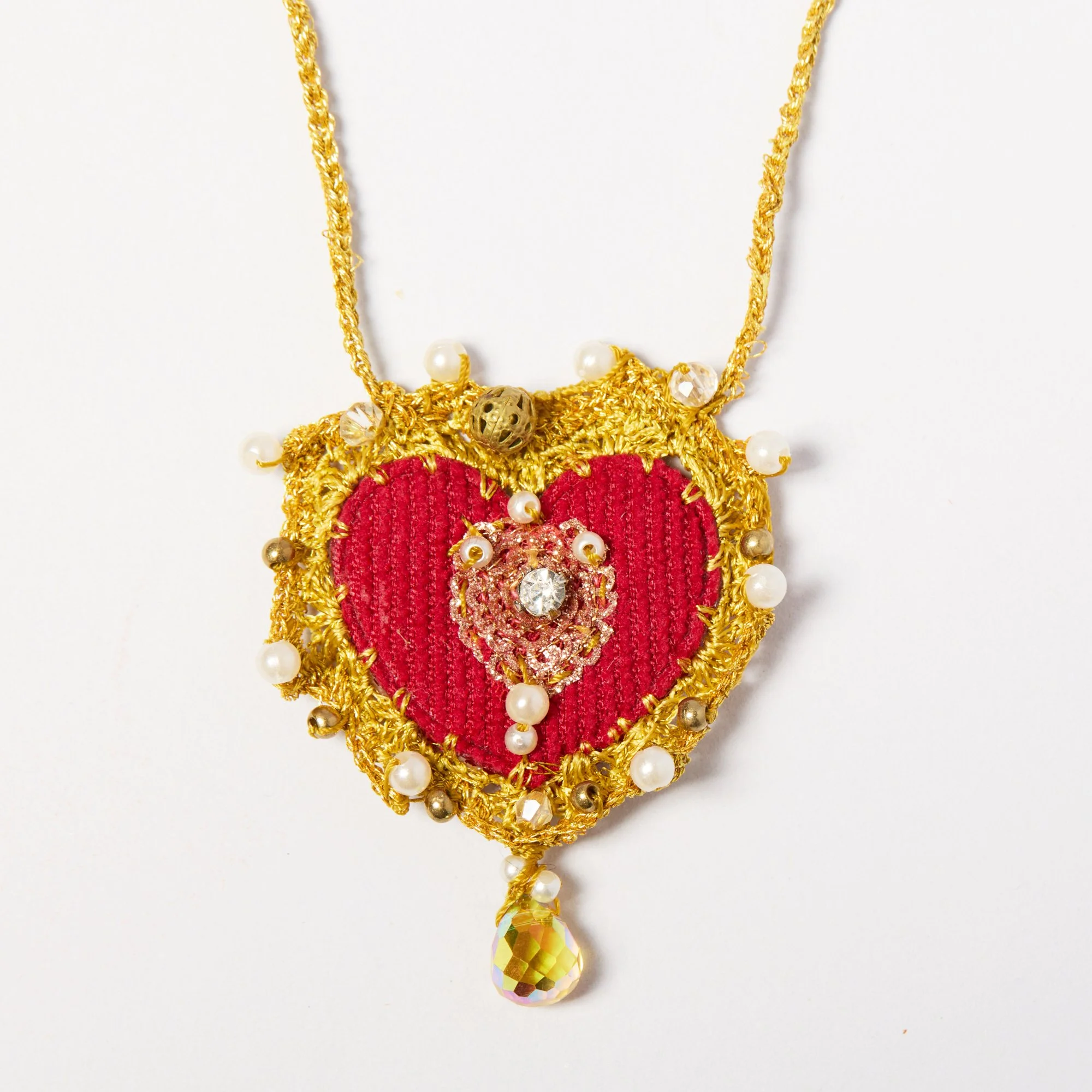 Close-up of a decorative gold necklace with pearls, beads, and a large iridescent drop-shaped pendant on a white background.