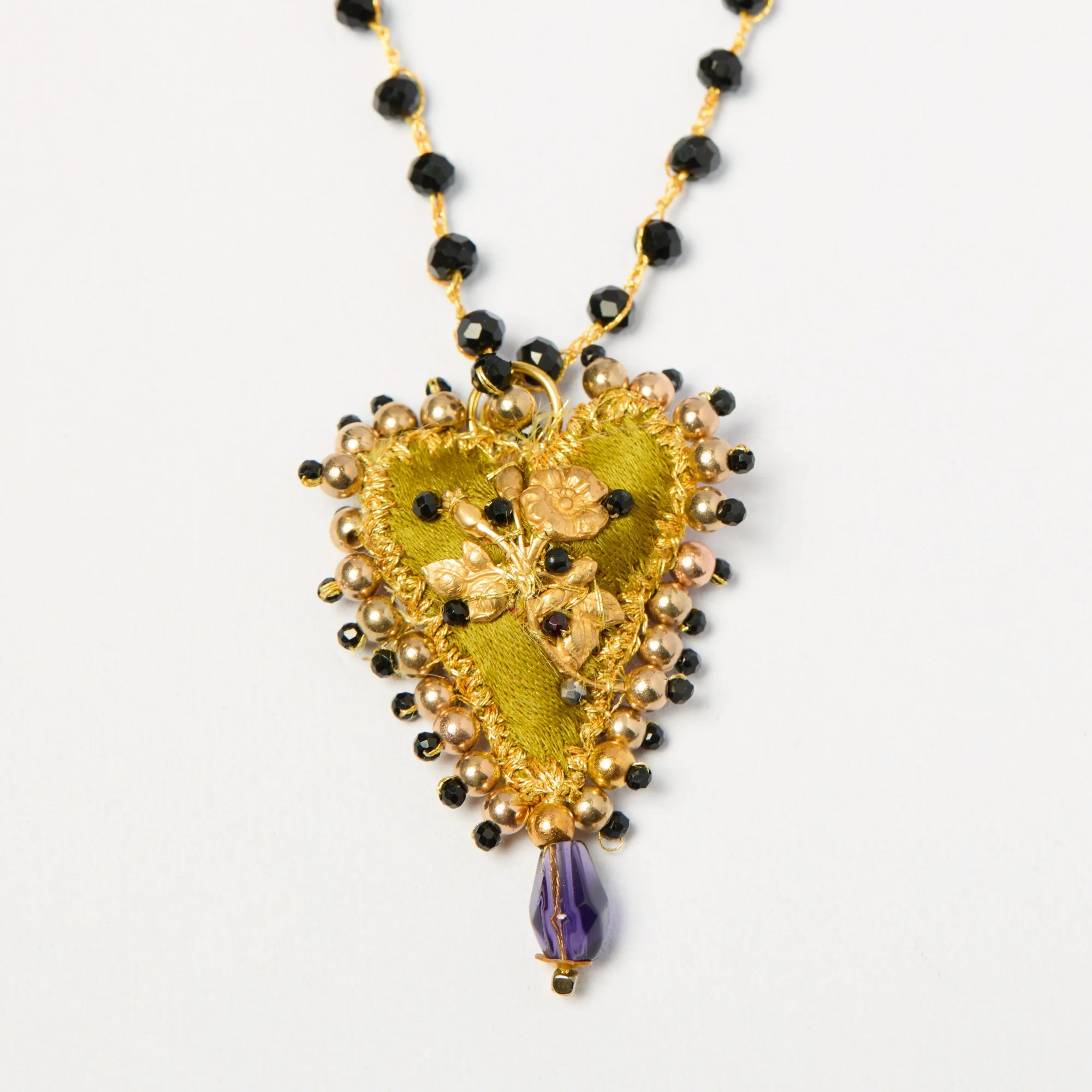 Close-up of a decorative hanging necklace with black beads, purple pendant, gold accents, and intricate design on a white background.