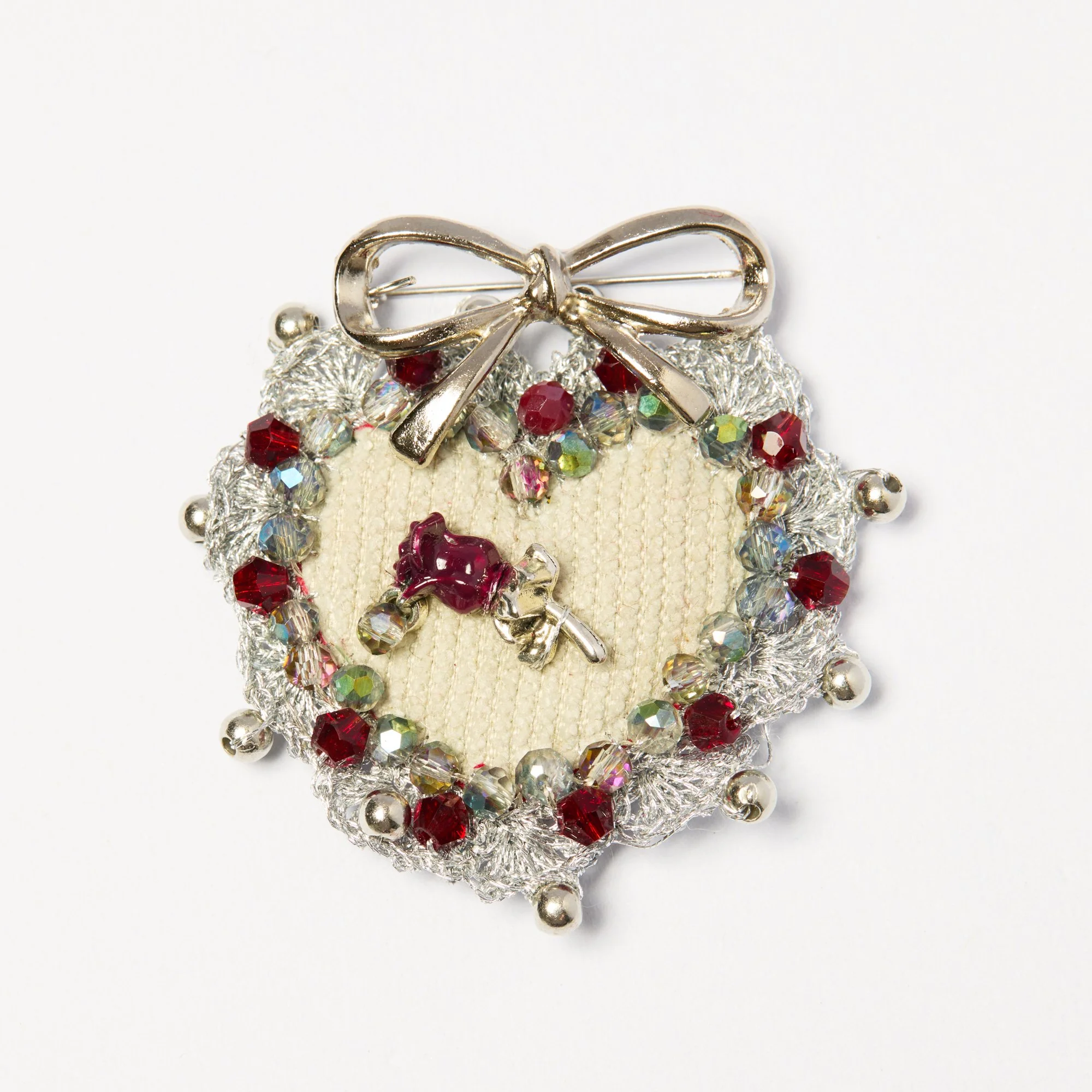 Close-up of a decorative brooch with a bow-shaped silver metal top and a cluster of red, clear, and iridescent beads and rhinestones on a white background.