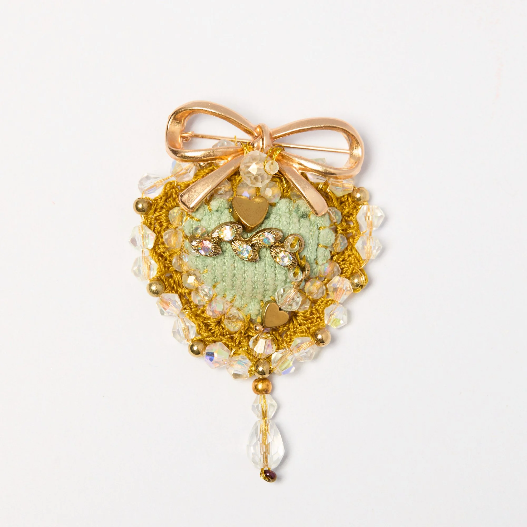 A decorative piece featuring a rose gold bow with beads and rhinestones, gold accents, and dangling crystal drops displayed against a plain white background.