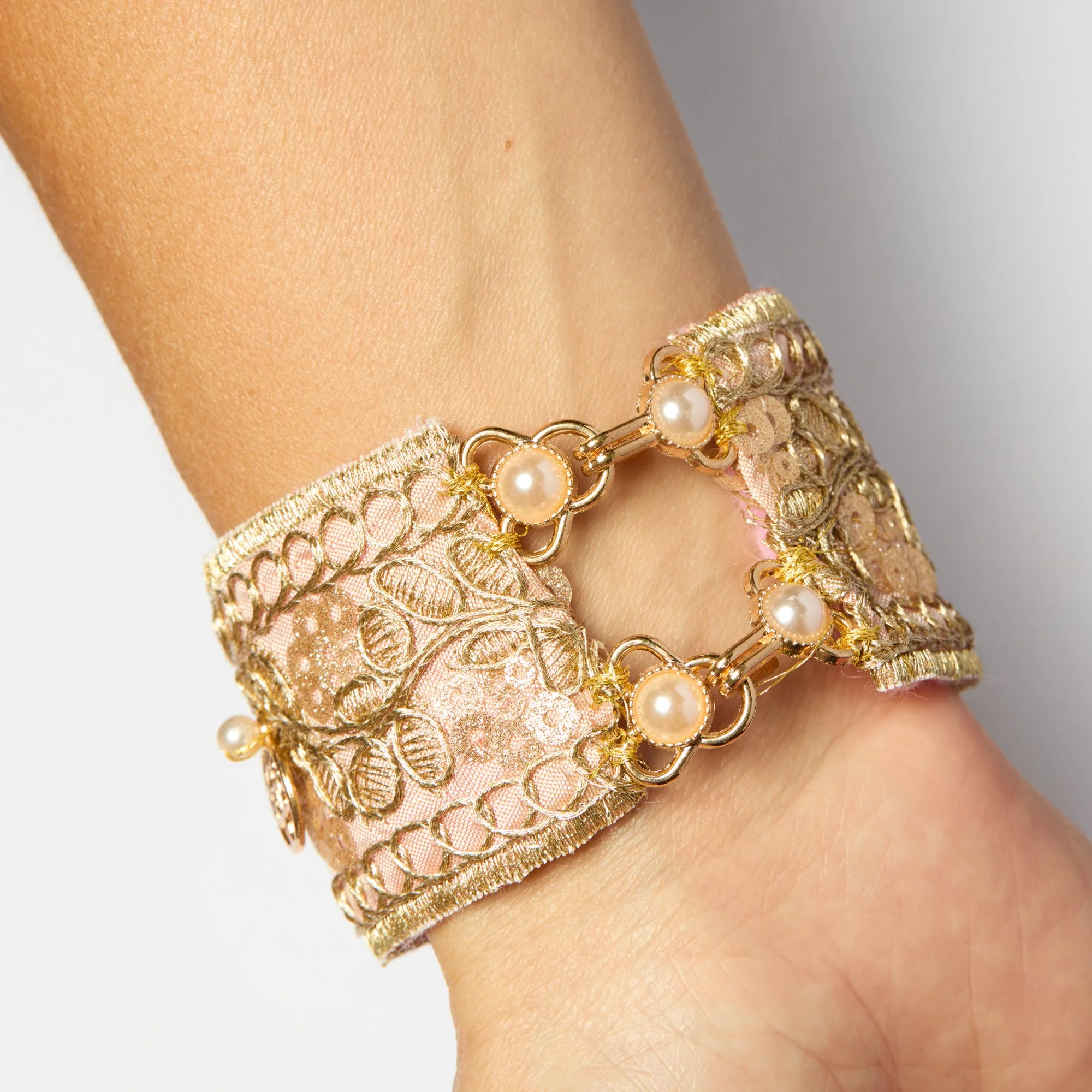Close-up of a person's wrist wearing gold jewelry bracelets with pearls.