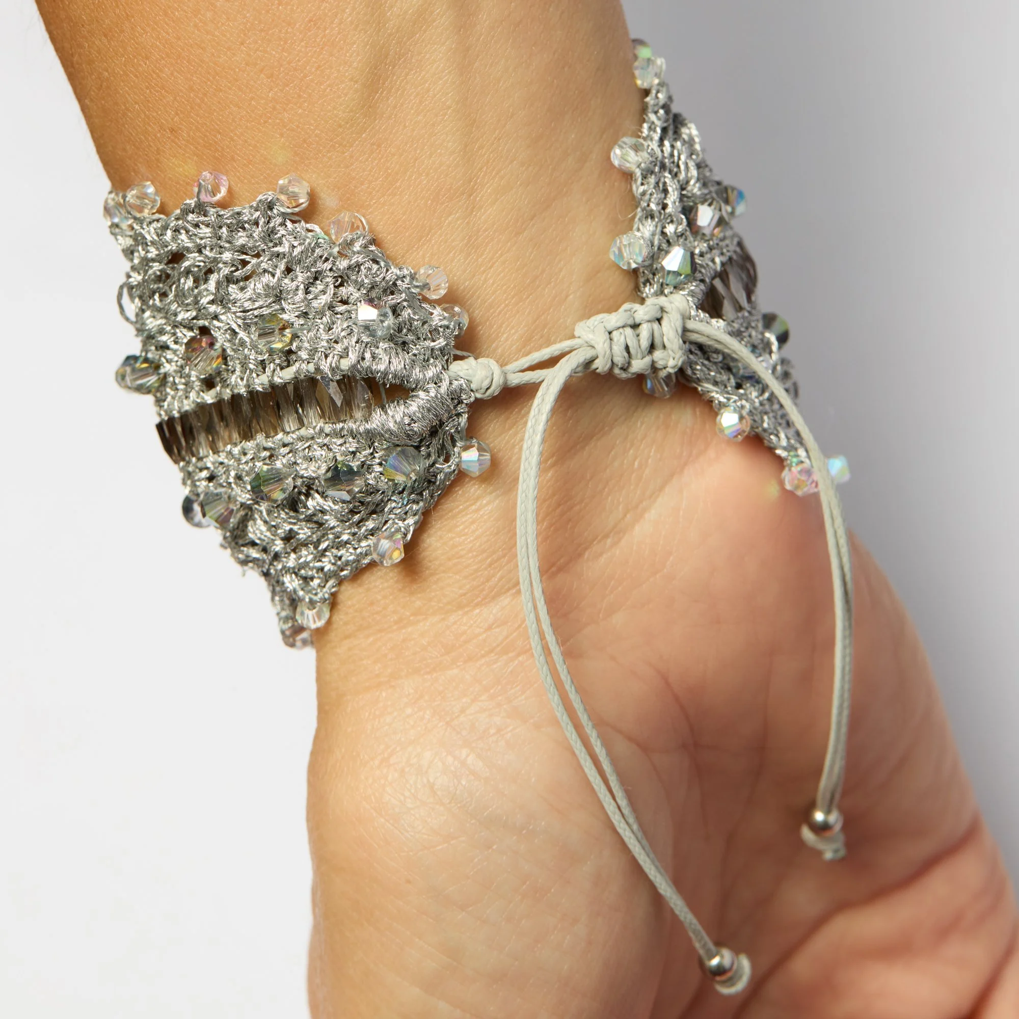 Close-up of a wrist wearing multiple silver and rhinestone bracelets and a white cord bracelet, with skin visible.