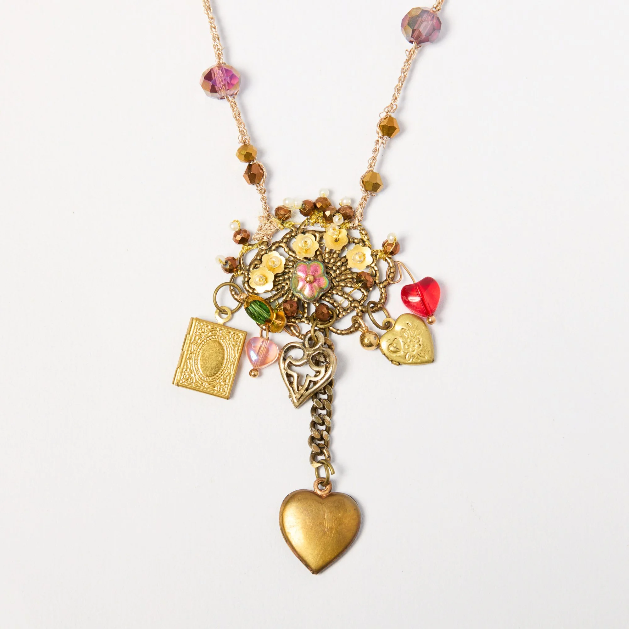 A gold-tone necklace with pink, amber, and pearl beads, and a large gold heart pendant on a white background.