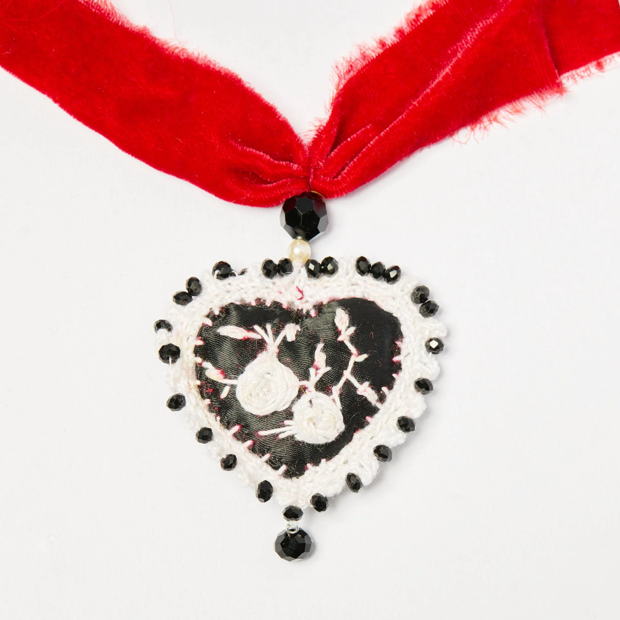 Close-up of a necklace with black beads, white crochet, and a large black and white skull charm on a white background.