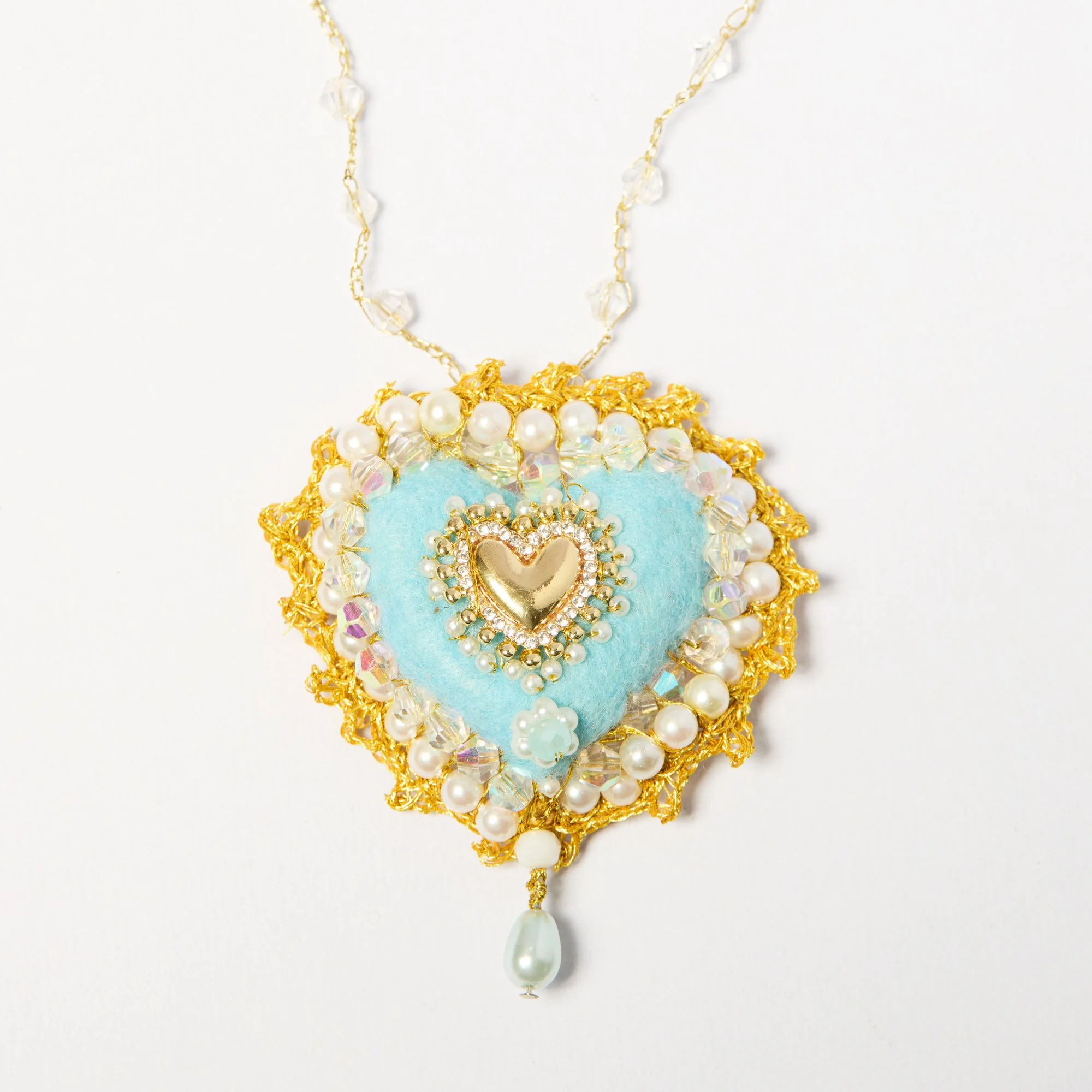 Close-up of an ornate necklace with gold and pearl embellishments, featuring a large teardrop pearl pendant at the bottom.