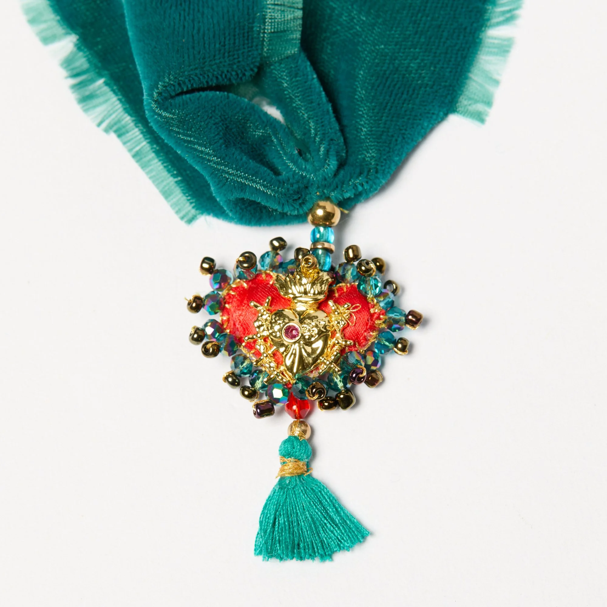 A decorative hanging ornament featuring teal fabric ribbons, beads, and a red fabric flower with a gold embellishment in the center, completed with a teal tassel at the bottom.