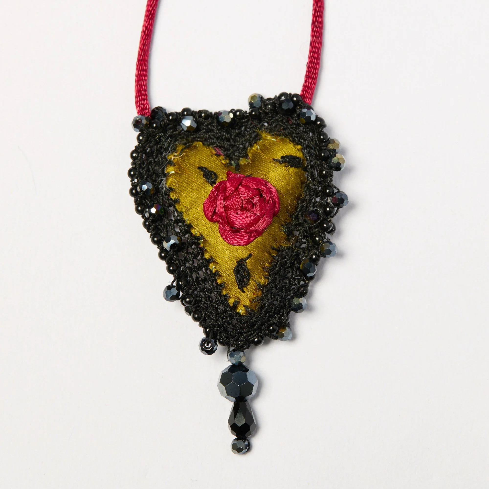 A handmade necklace with black beads, a yellow fabric heart with black thread details, and a red satin thread.