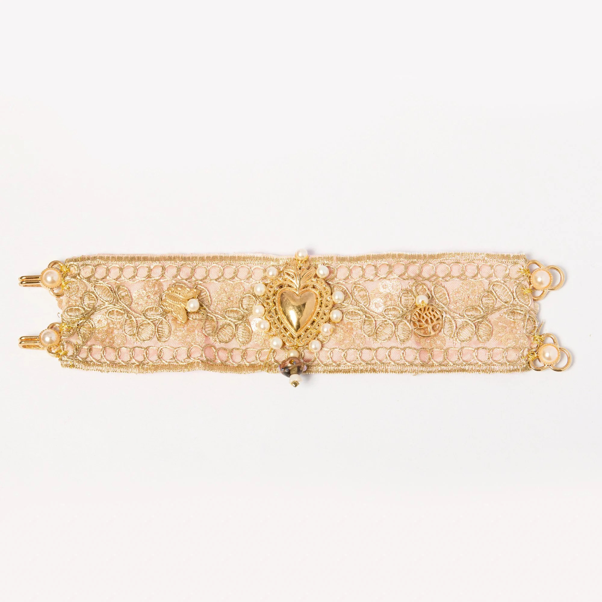 A decorative pink lace choker necklace with a gold heart-shaped pendant and pearl embellishments on a white background.