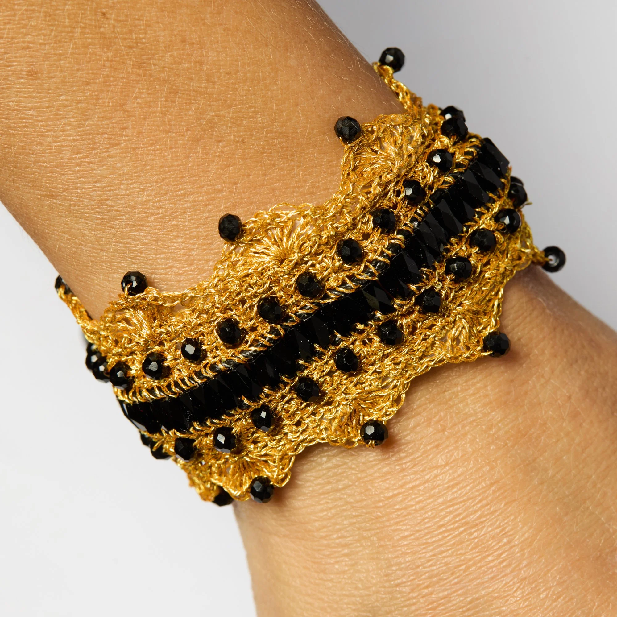 Close-up of a wrist adorned with multiple gold and black beaded bracelets with intricate woven details.