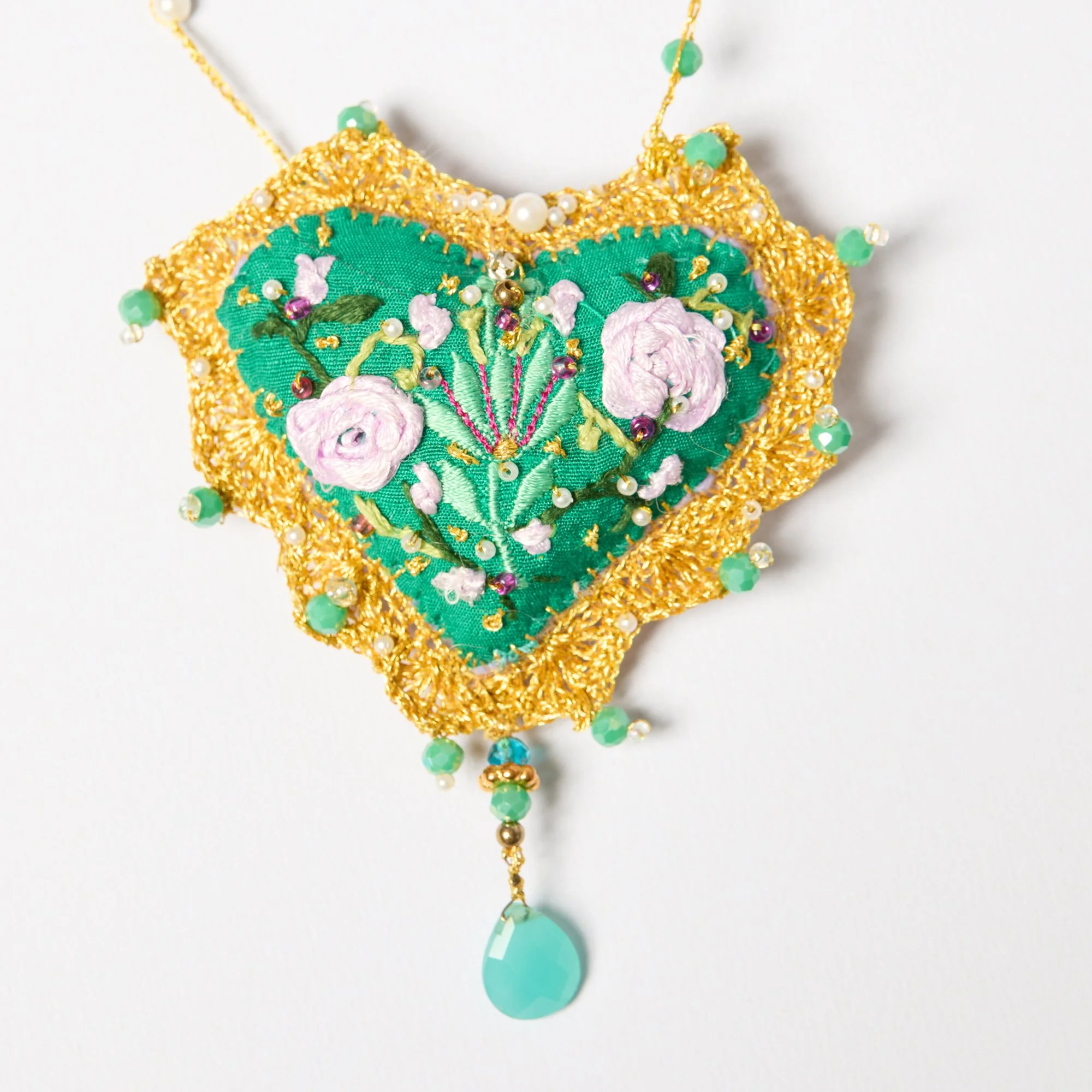Close-up of an ornate necklace with gold, green, white, and purple beads, featuring a floral and fan embroidery design.