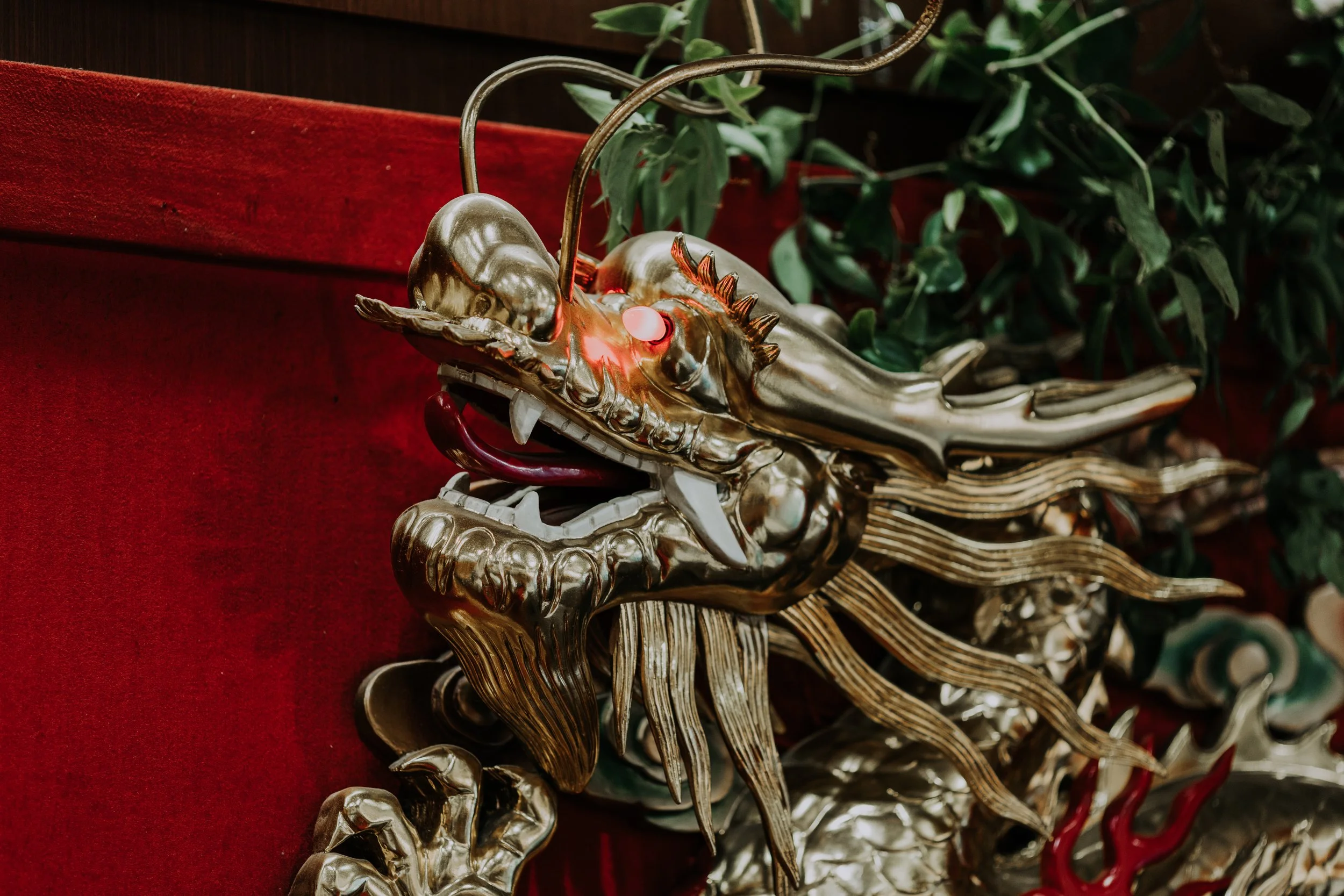 A metallic dragon costume or sculpture with intricate detailing, placed on a red surface with green foliage in the background.