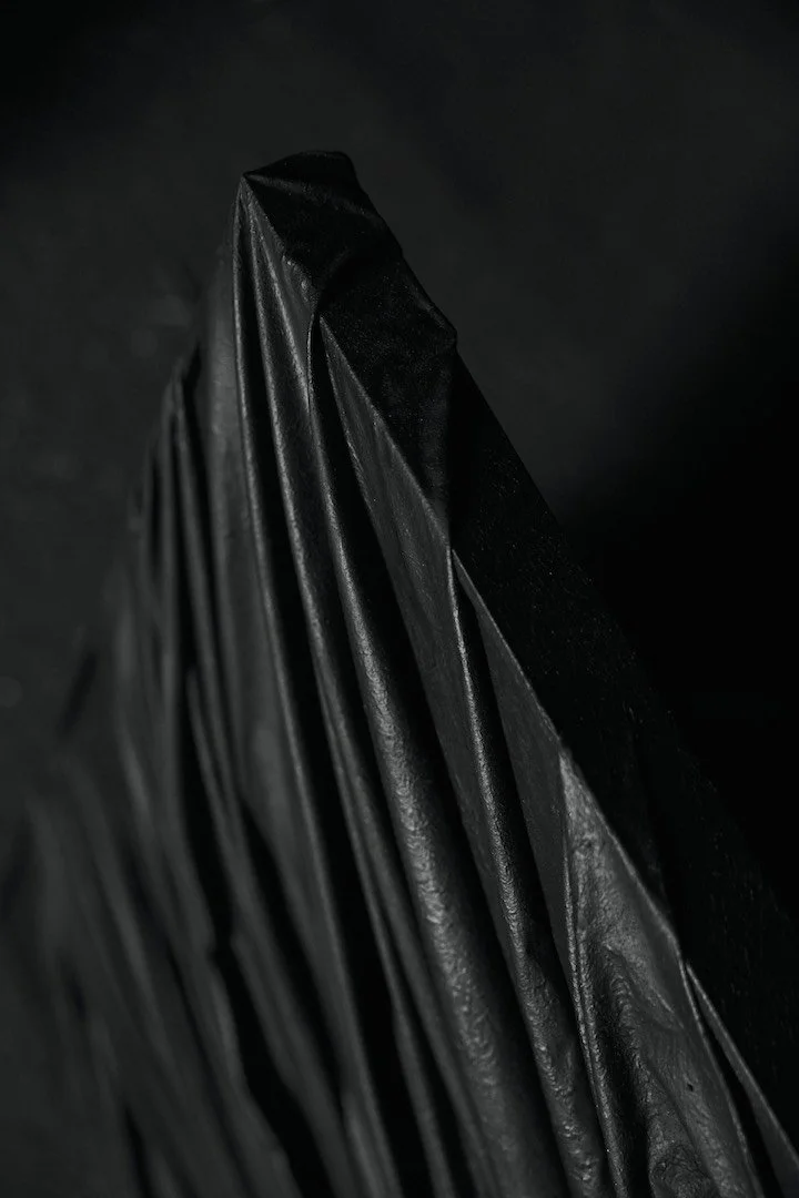 Close-up of a black, shiny, pleated fabric or material against a dark background.