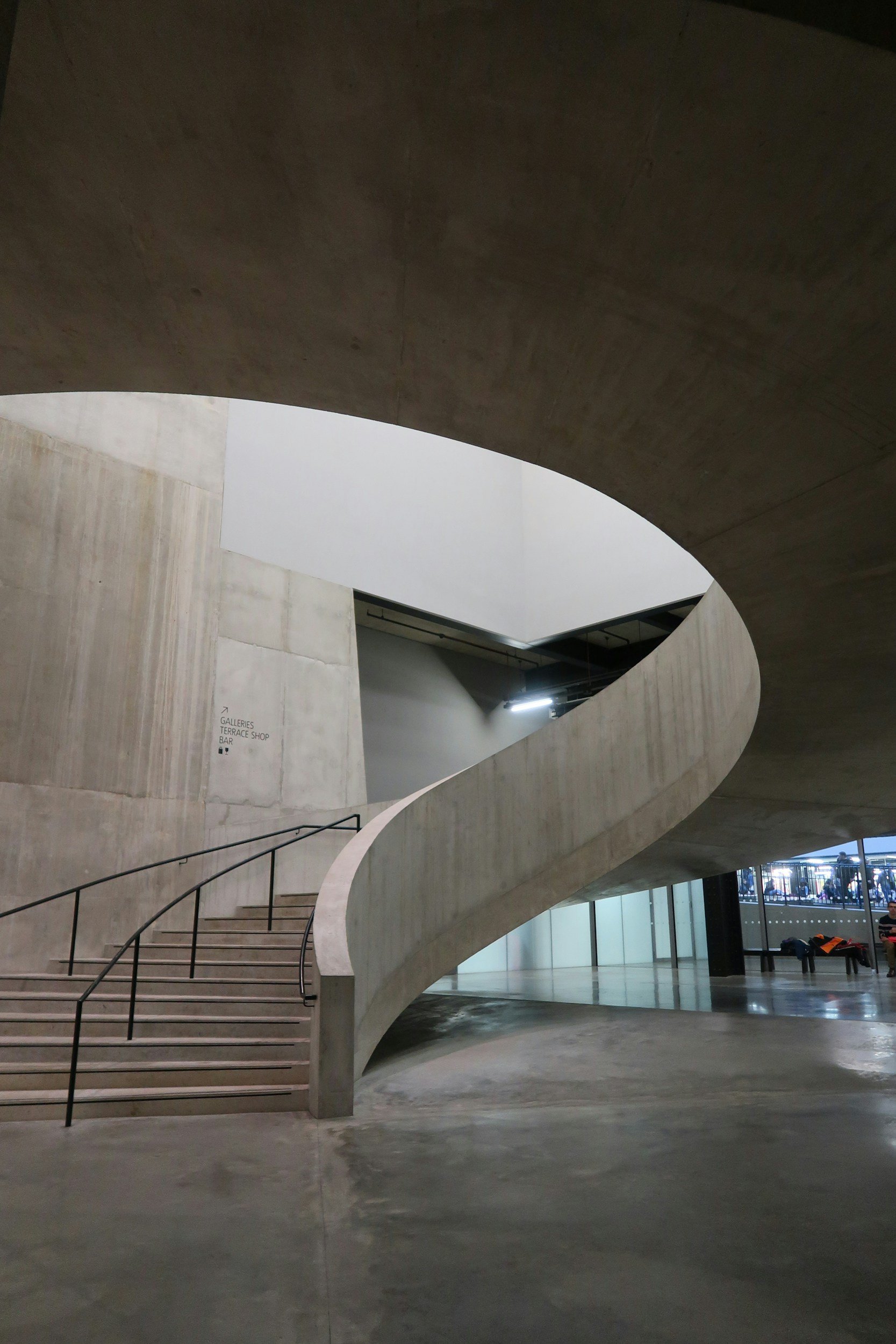 Modern indoor space with a curved concrete staircase, glass doors, and minimalistic design.