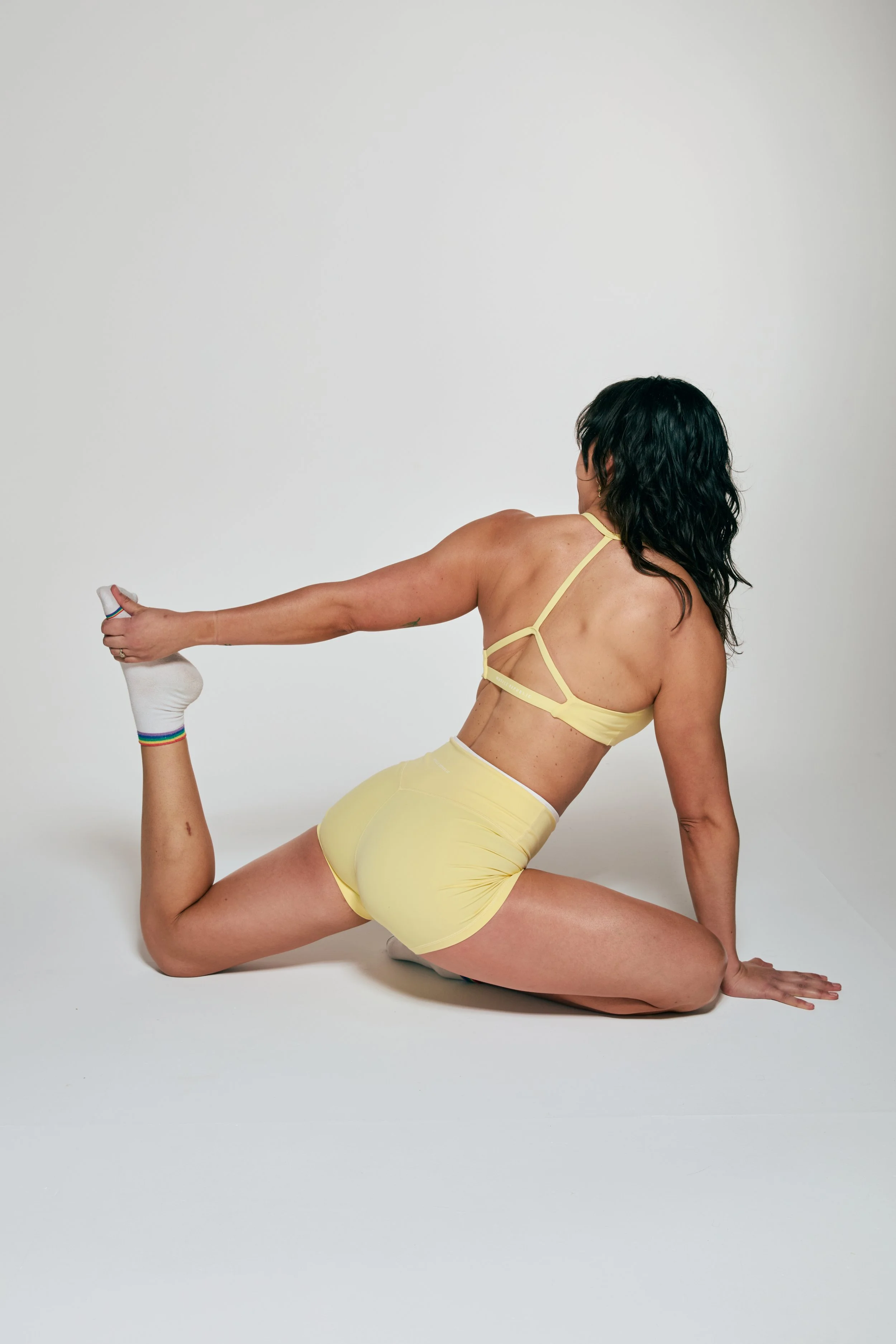 A woman in yellow workout attire performing a yoga pose on a white background.