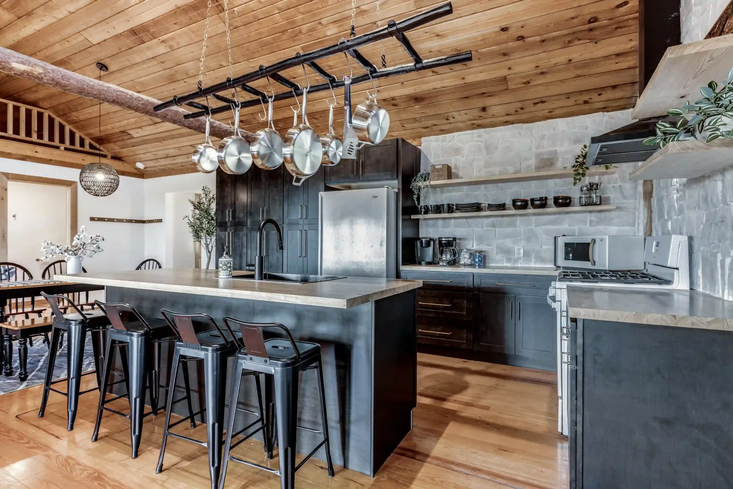 Kitchen with wooden ceiling, hanging pots on a rack, black cabinets, and stainless steel appliances.