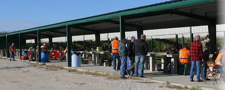 People at a covered outdoor shooting range with firearms and targets.