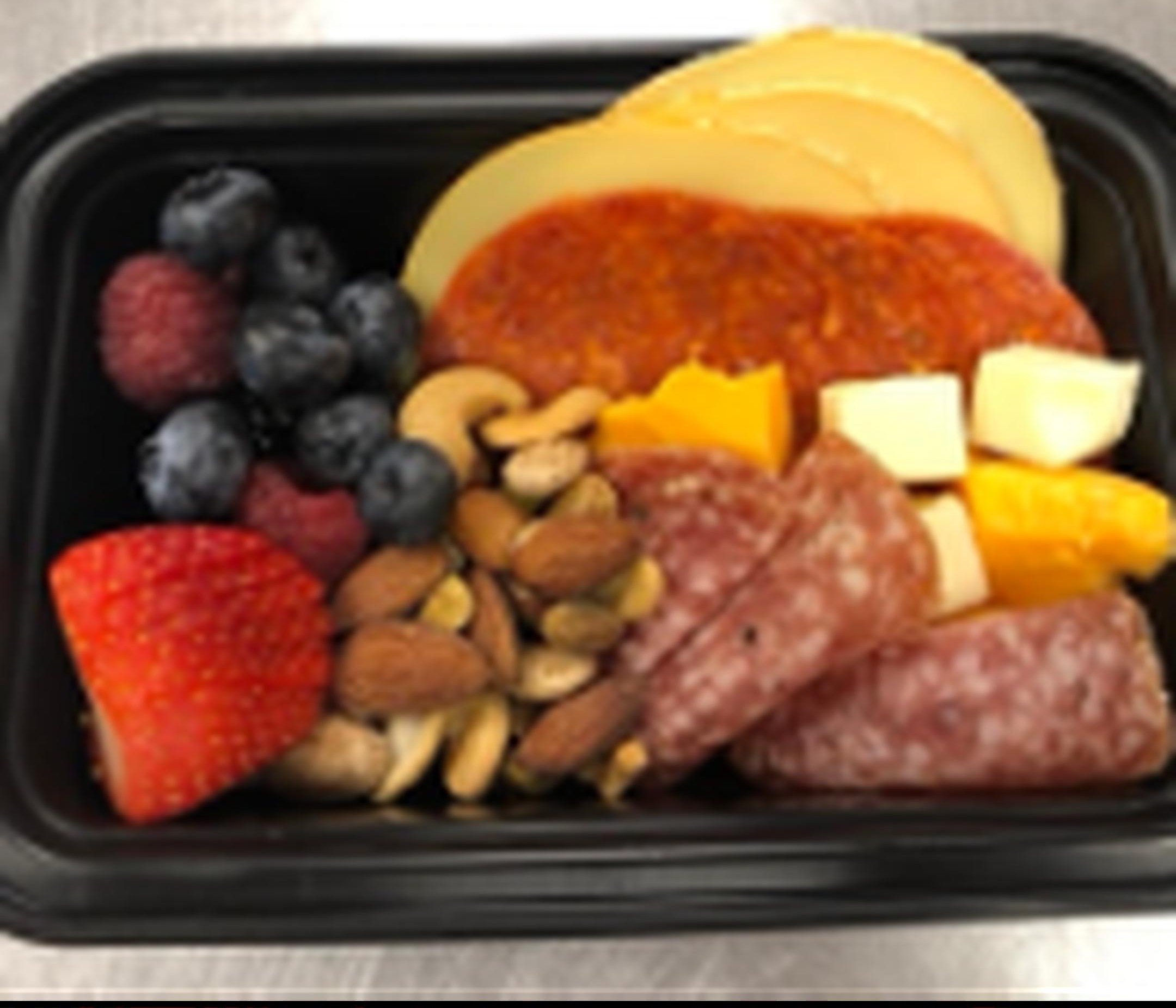 Assorted sliced fruits and meat in a black plastic container.