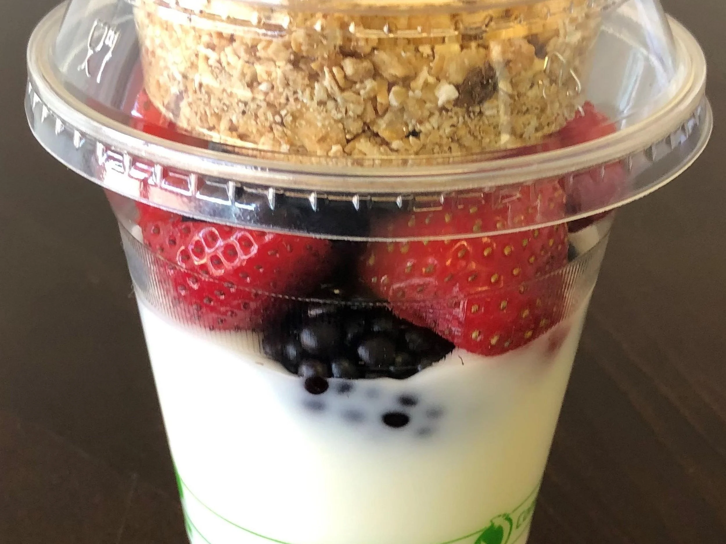 Close-up of a dessert parfait with layers of granola, blueberries, and yogurt in a clear plastic cup.