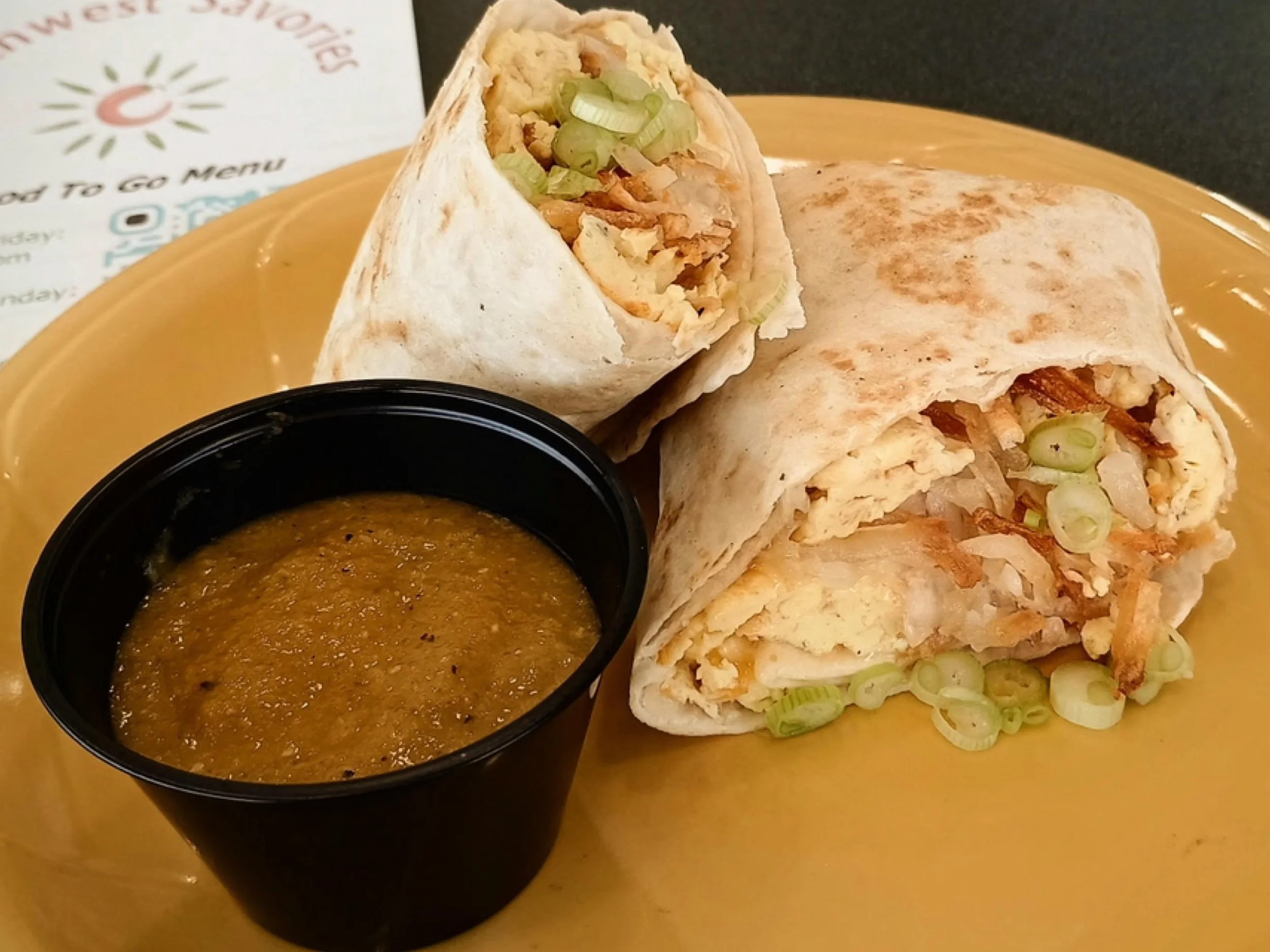 A plate with two chicken and scallion wraps and a cup of brown dipping sauce.